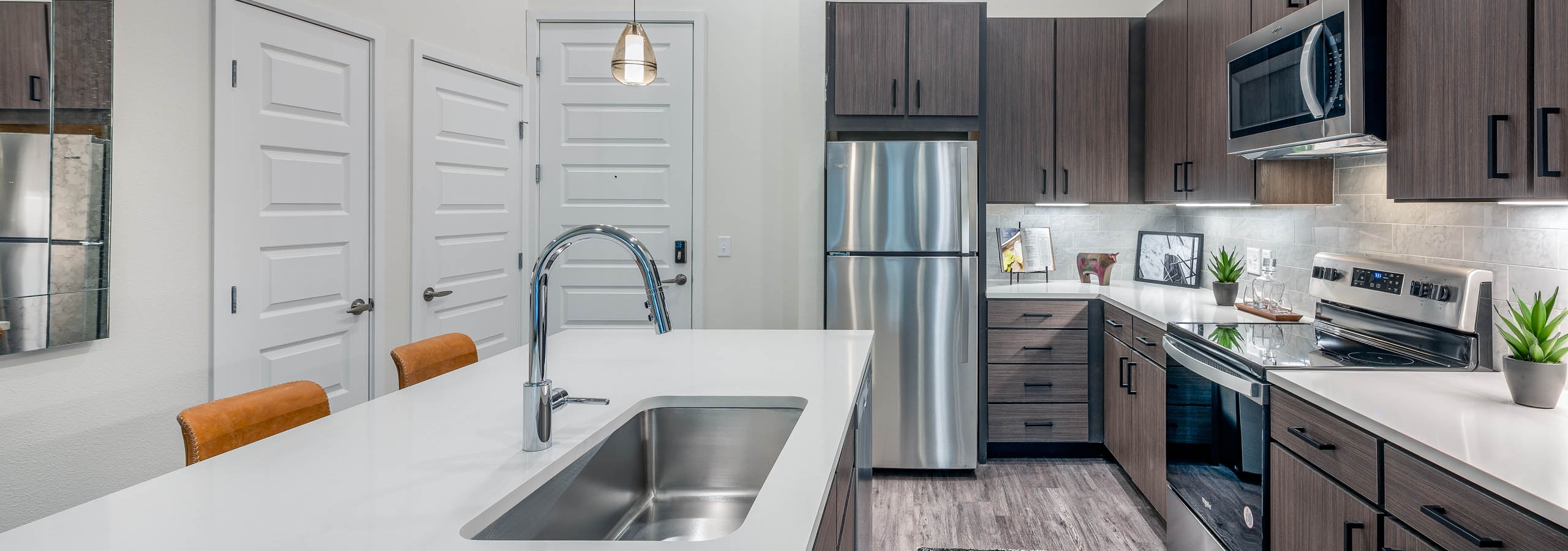 Interior view of a kitchen at AMLI Art District with quartz countertops and tan tile backsplash and view of the living room