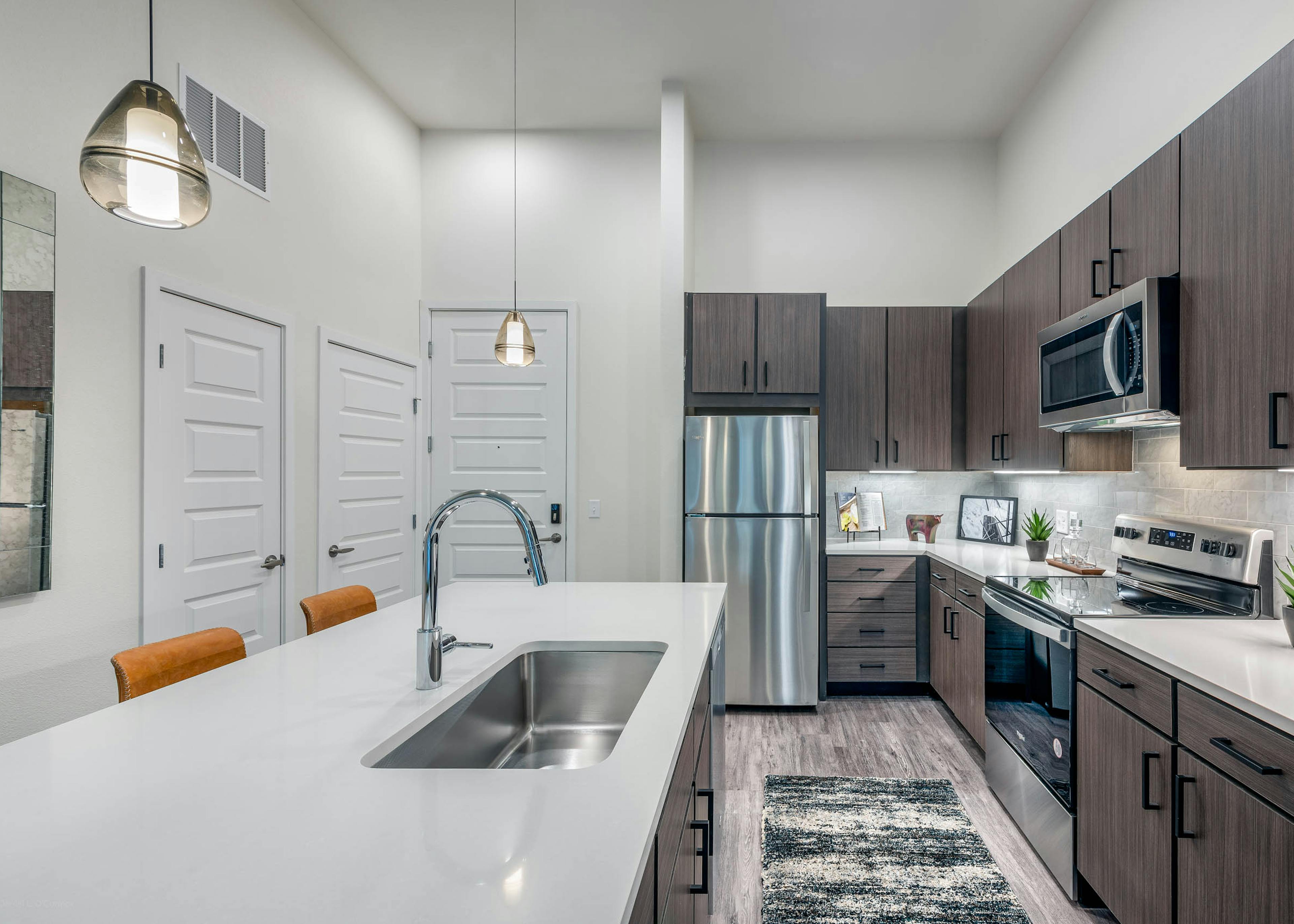 Interior view of a kitchen at AMLI Art District with quartz countertops and tan tile backsplash and view of the living room