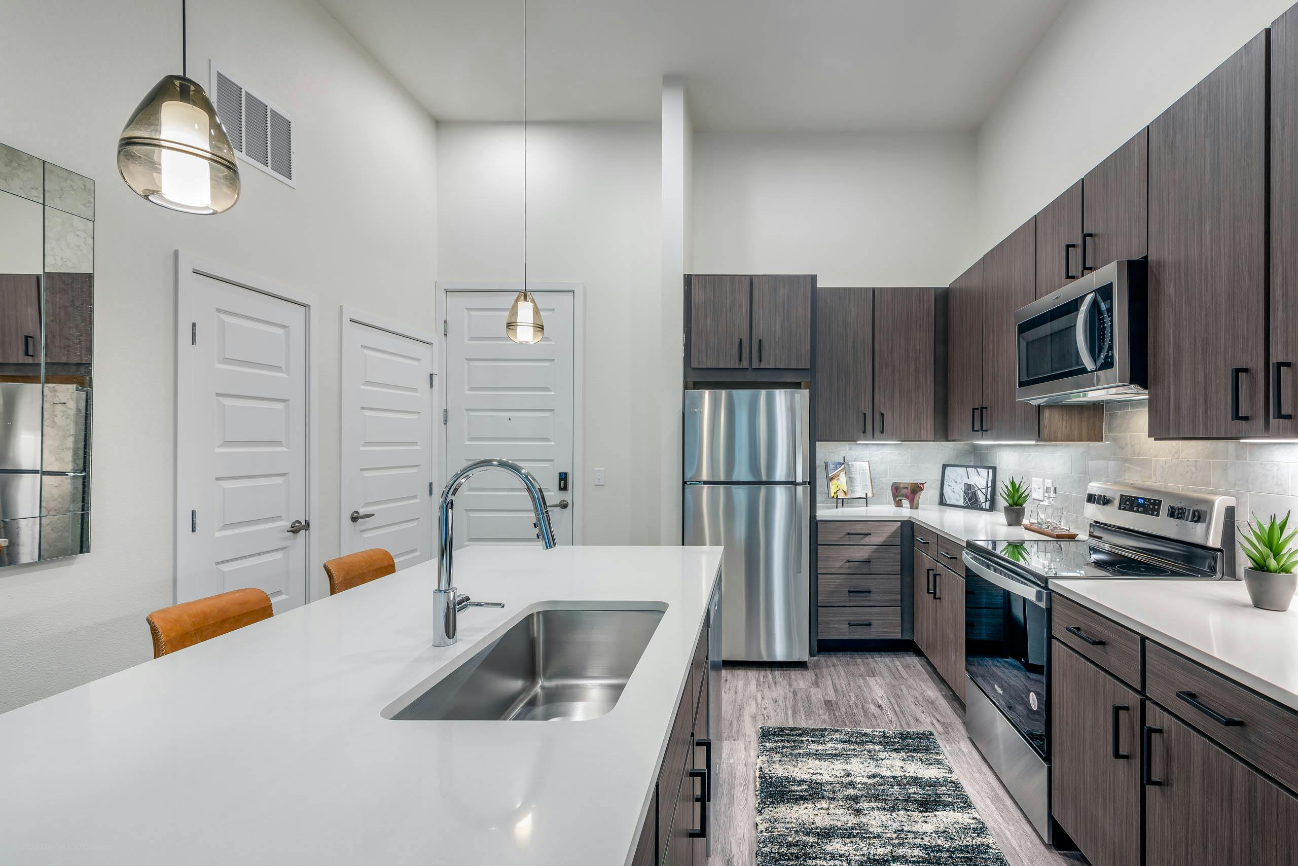 Interior view of a kitchen at AMLI Art District with quartz countertops and tan tile backsplash and view of the living room