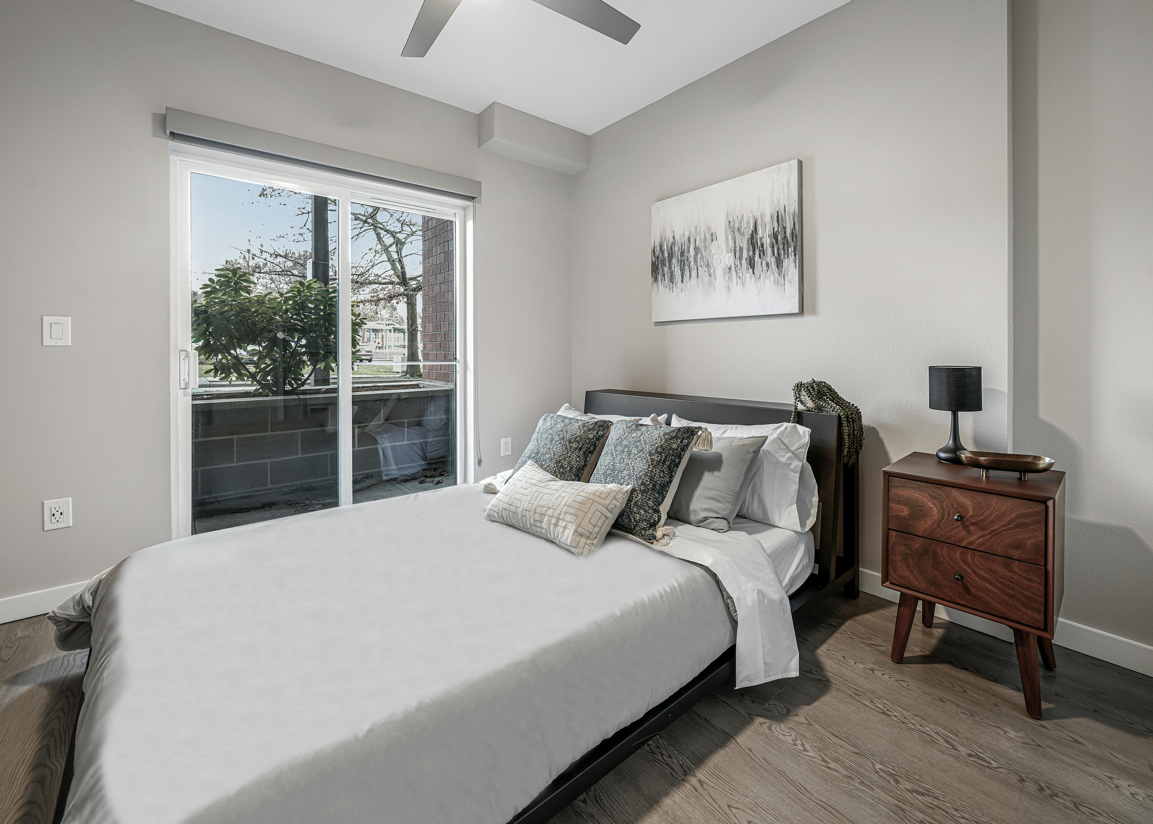 AMLI Bellevue Park apartment bedroom with white and grey bed and brown nightstand and sliding glass door to patio