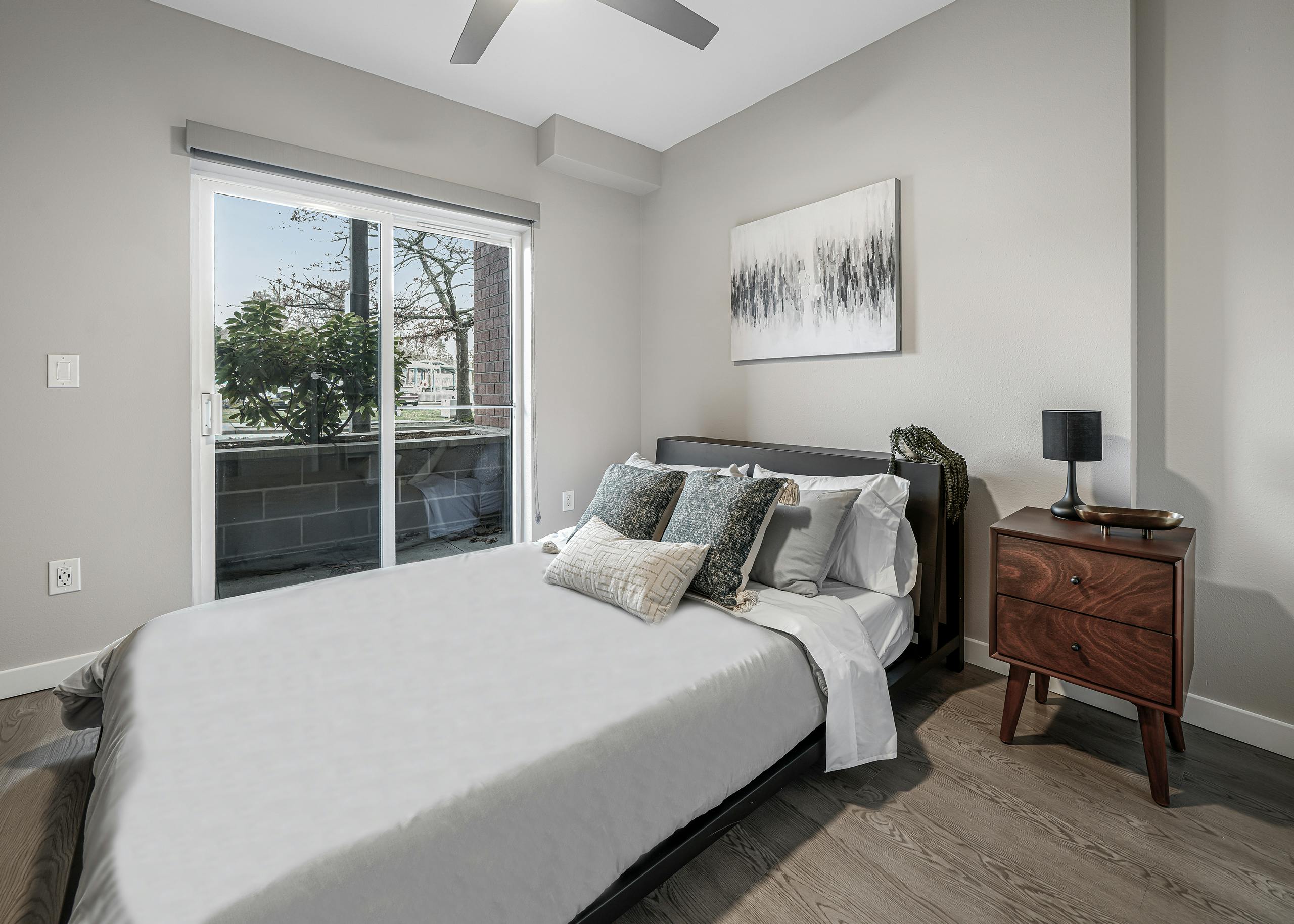 AMLI Bellevue Park apartment bedroom with white and grey bed and brown nightstand and sliding glass door to patio