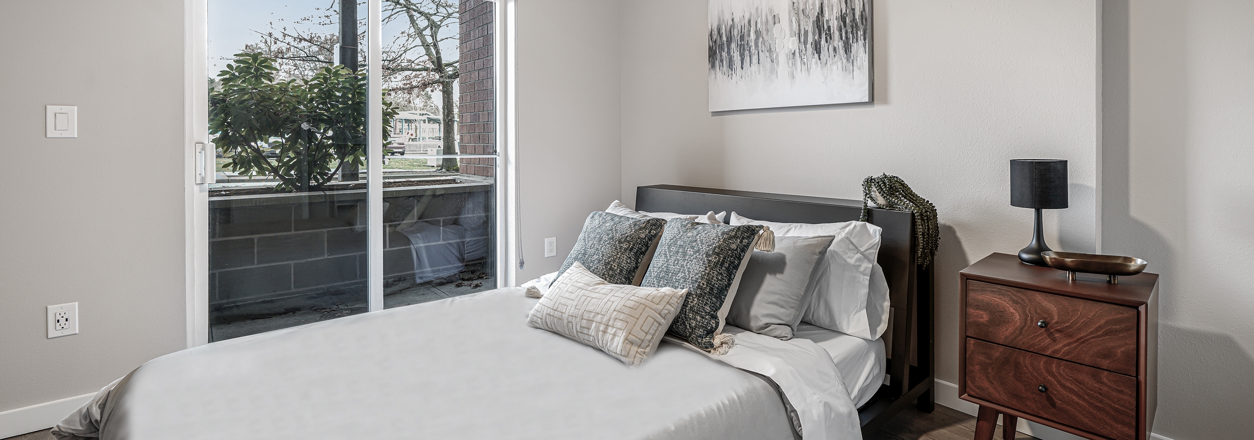 AMLI Bellevue Park apartment bedroom with white and grey bed and brown nightstand and sliding glass door to patio