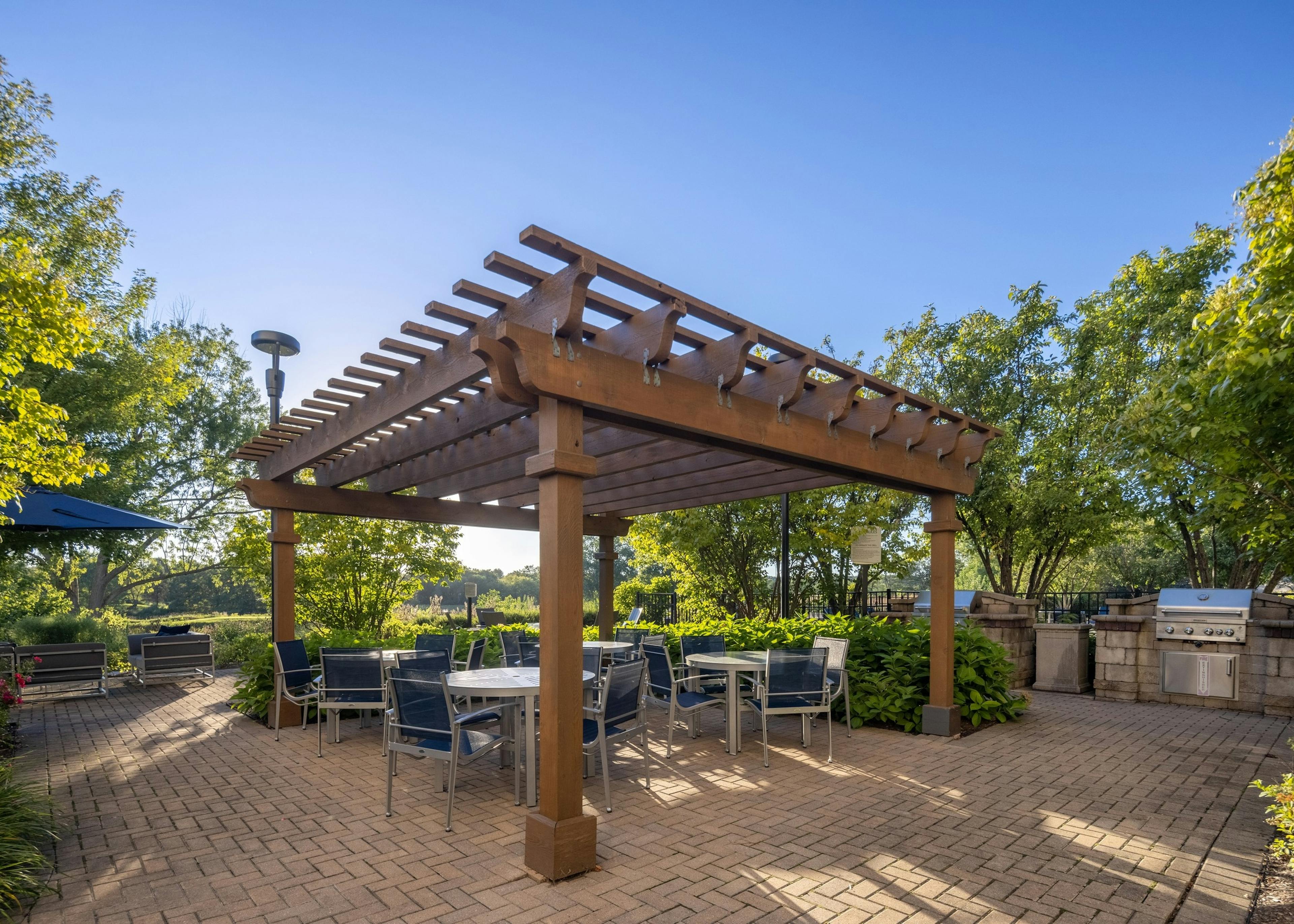 Dual grill station at AMLI at Seven Bridges with tables and hairs under a wood trellis surrounded by green vibrant trees