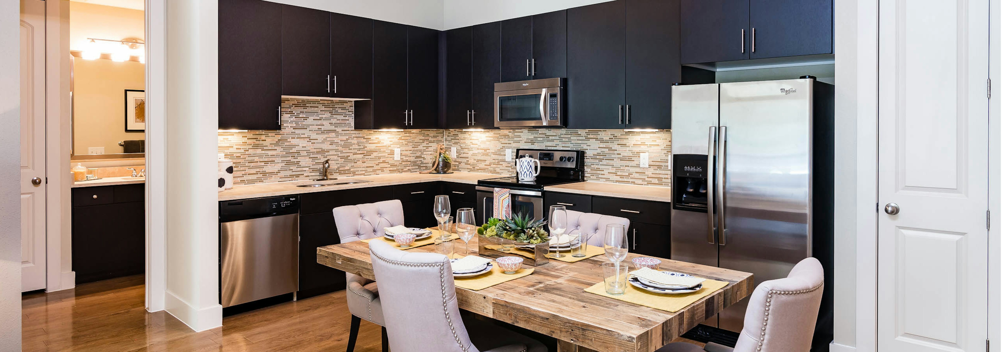 Interior view of AMLI RidgeGate dining area with table fully set and kitchen with dark cabinets and mosaic tile backsplash