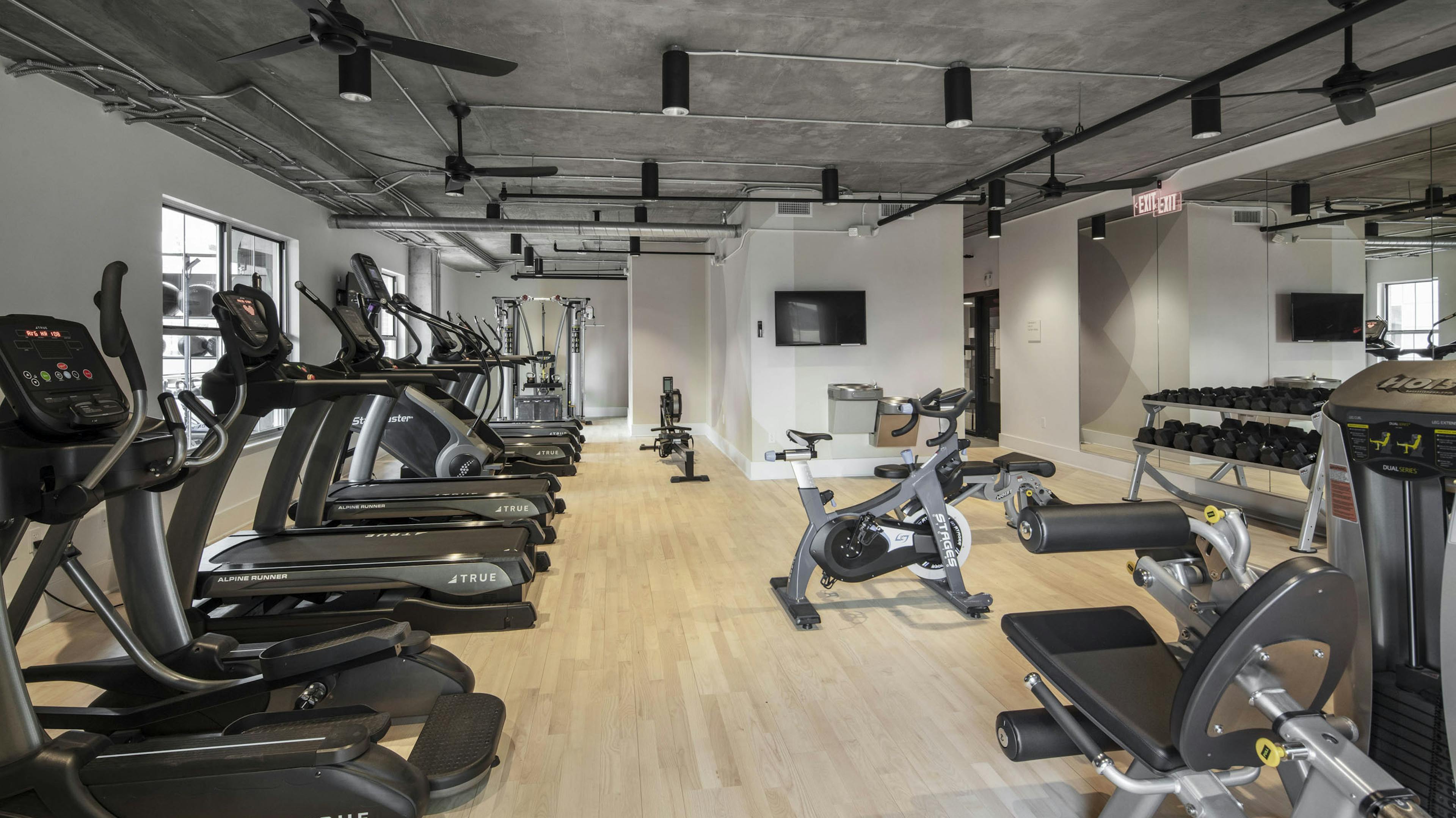 AMLI Downtown fitness center with cardio and strength training machines with wood floor and concrete ceiling with ceiling fans