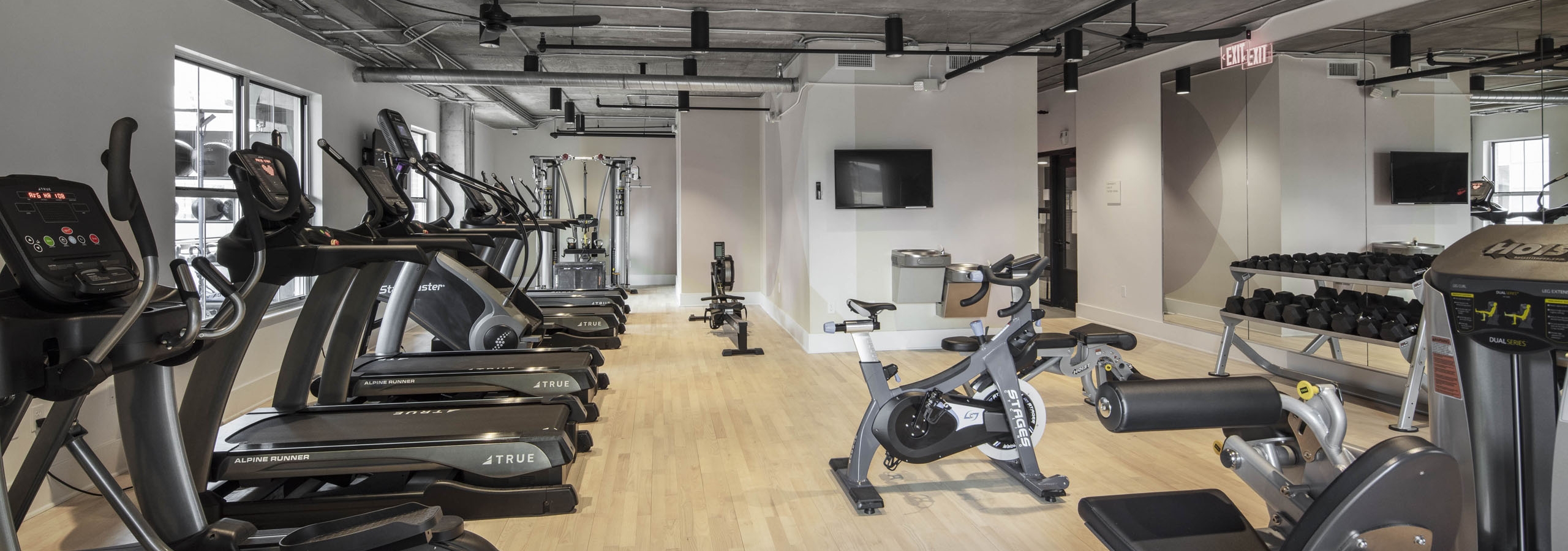 AMLI Downtown fitness center with cardio and strength training machines with wood floor and concrete ceiling with ceiling fans