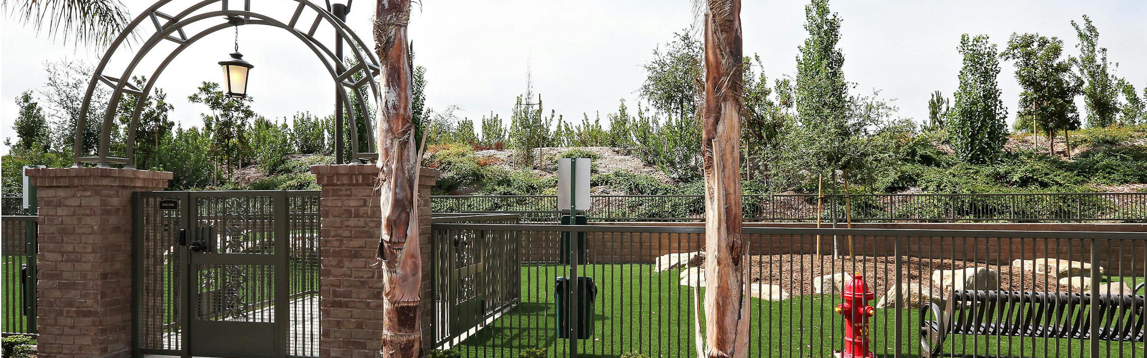 Daytime view of Dog Park’s arched entrance with fence, turf and pet waste station at AMLI Spanish Hills apartment building