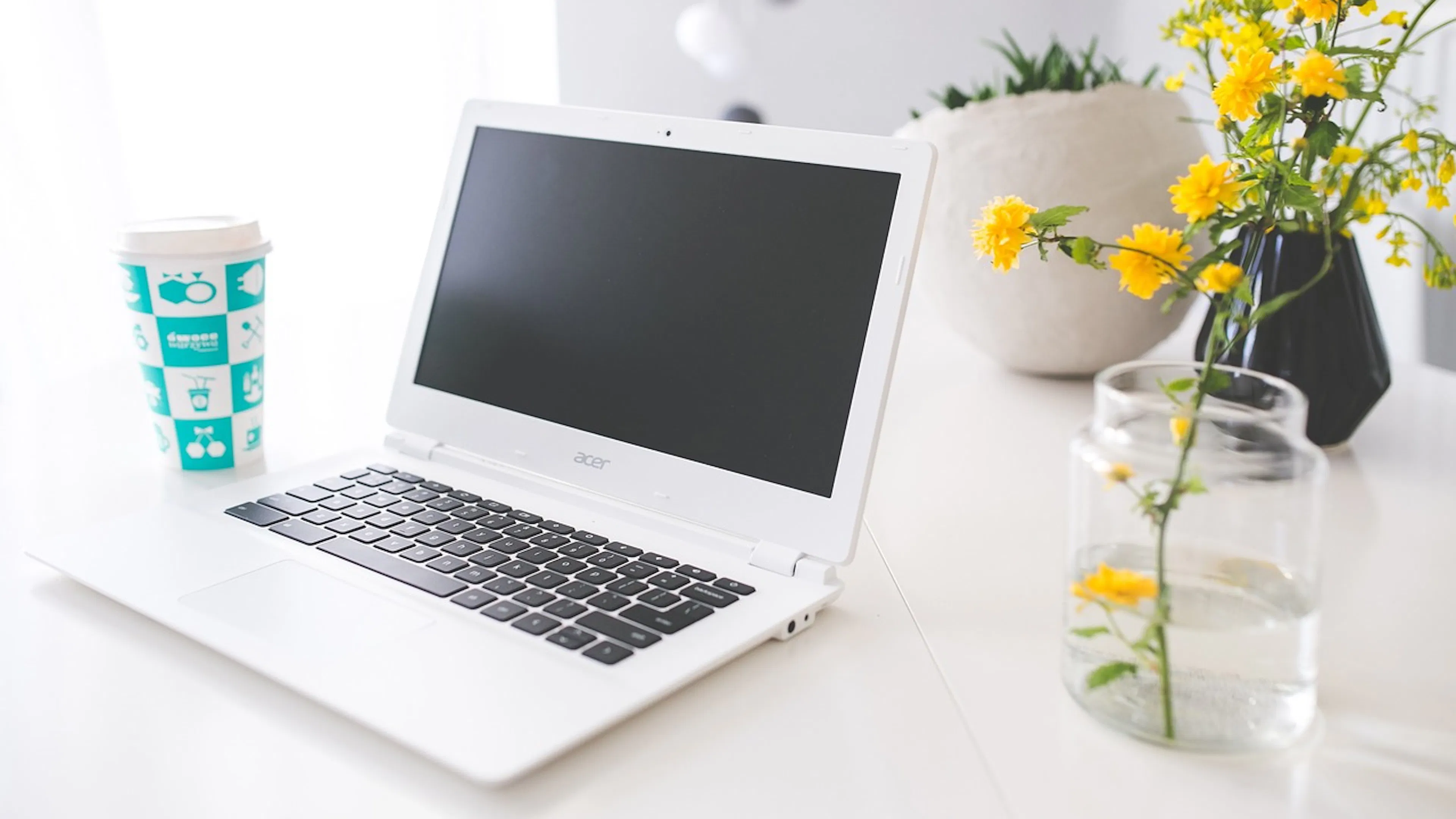 white laptop with yellow flowers in vase beside a cup of coffee