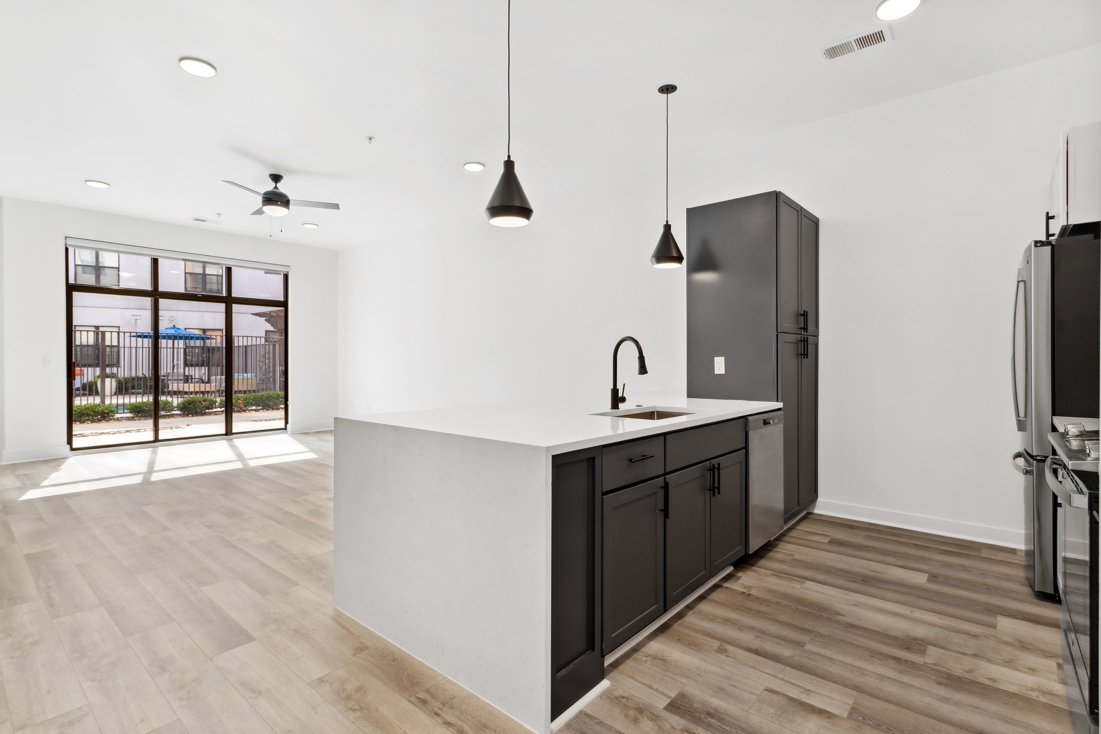 Living room and kitchen with black cabinets and white countertops and black hanging pendent lights at AMLI Old 4th Ward