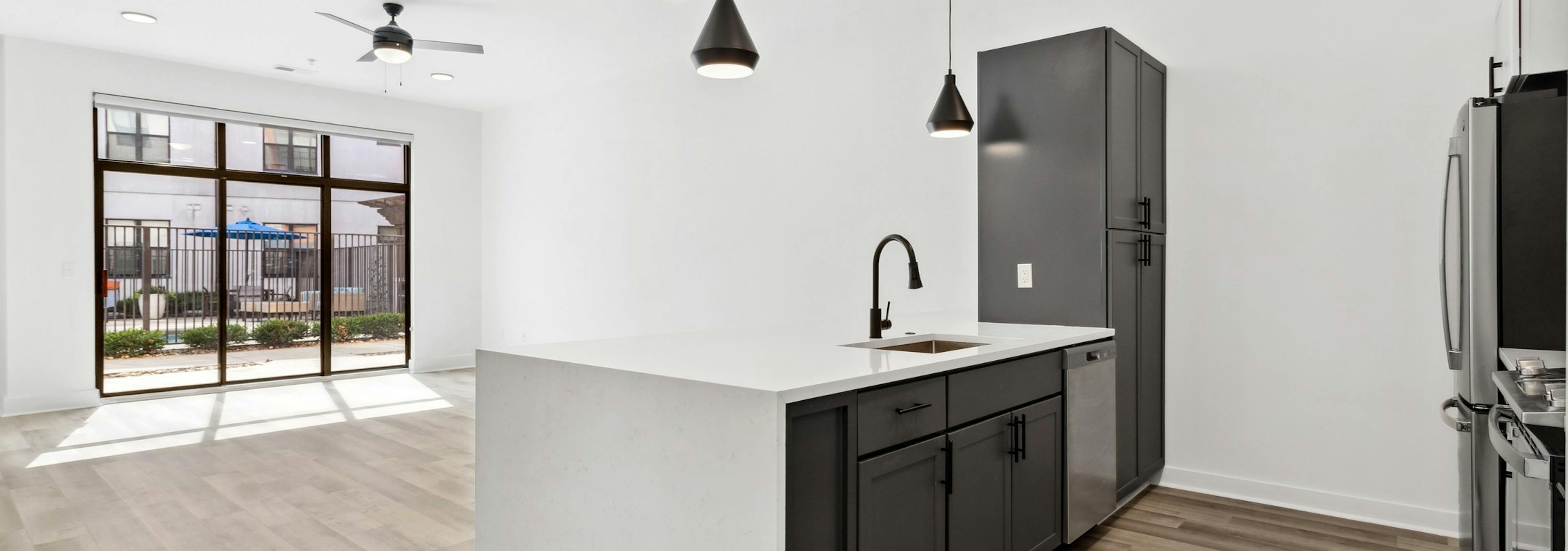 Living room and kitchen with black cabinets and white countertops and black hanging pendent lights at AMLI Old 4th Ward