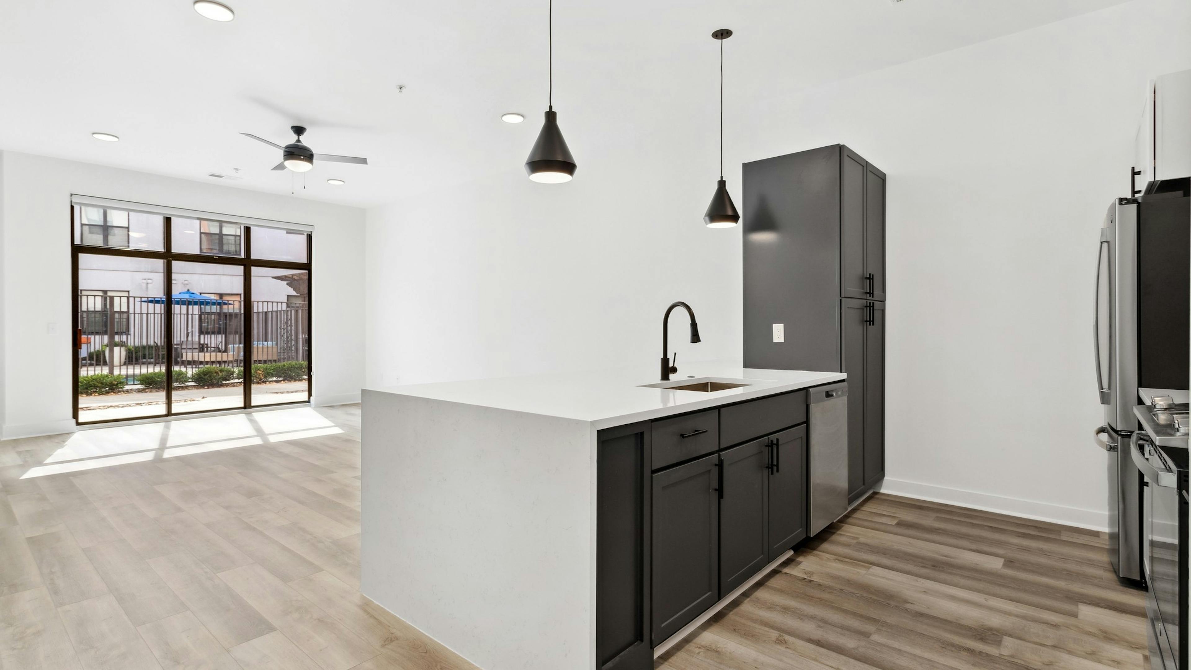 Living room and kitchen with black cabinets and white countertops and black hanging pendent lights at AMLI Old 4th Ward