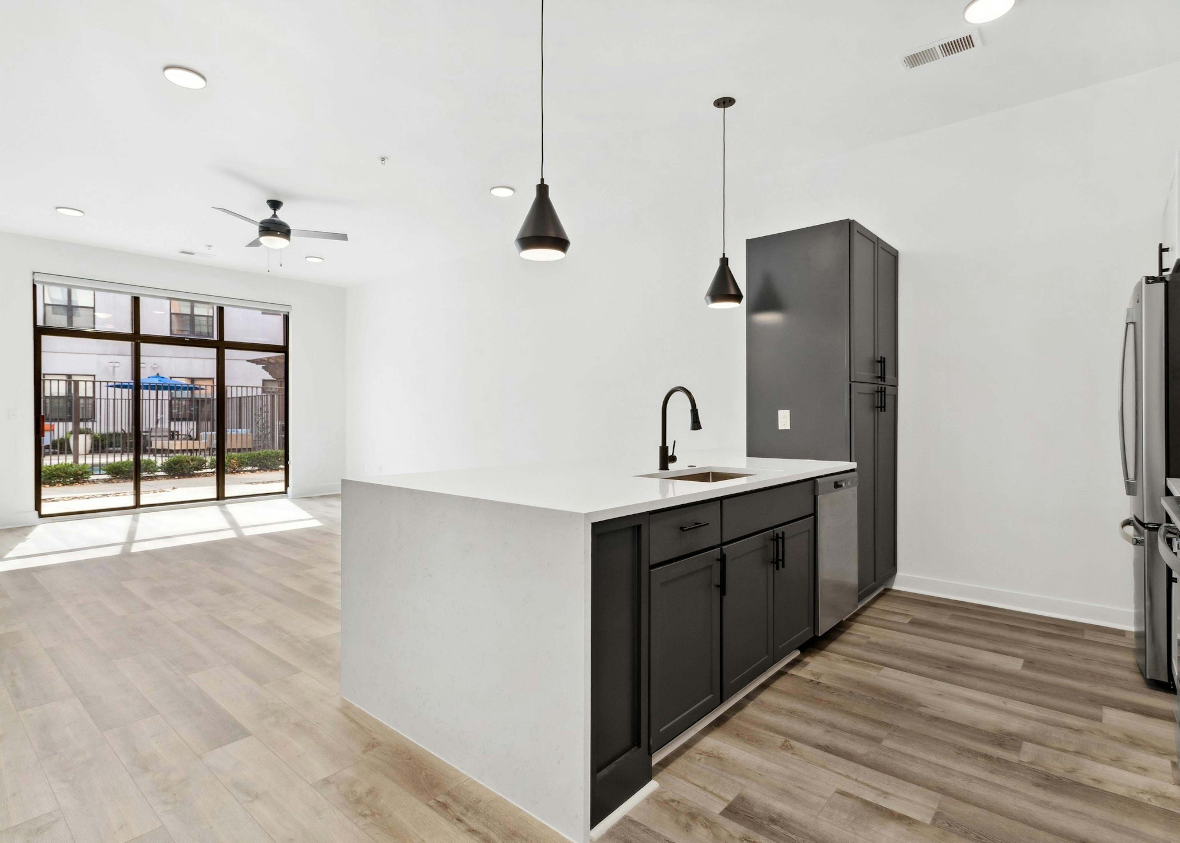 Living room and kitchen with black cabinets and white countertops and black hanging pendent lights at AMLI Old 4th Ward