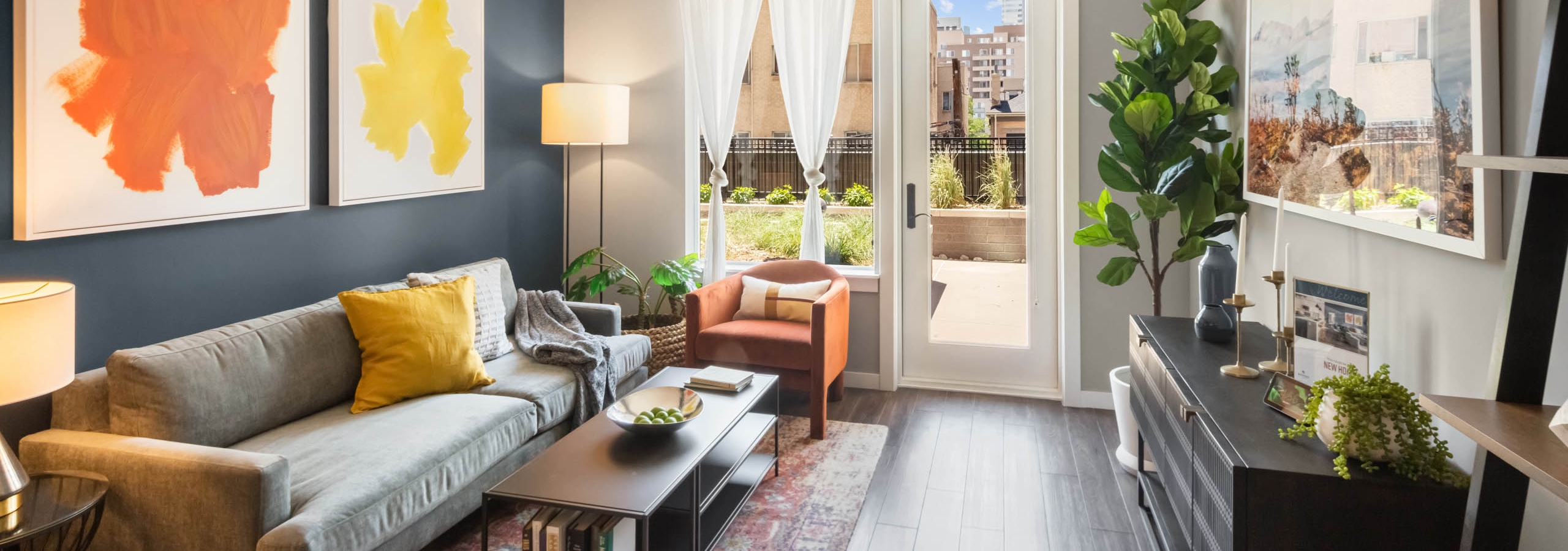 Bright AMLI at Uptown apartment living room with orange and yellow artwork on dark blue accent wall and door leading to patio