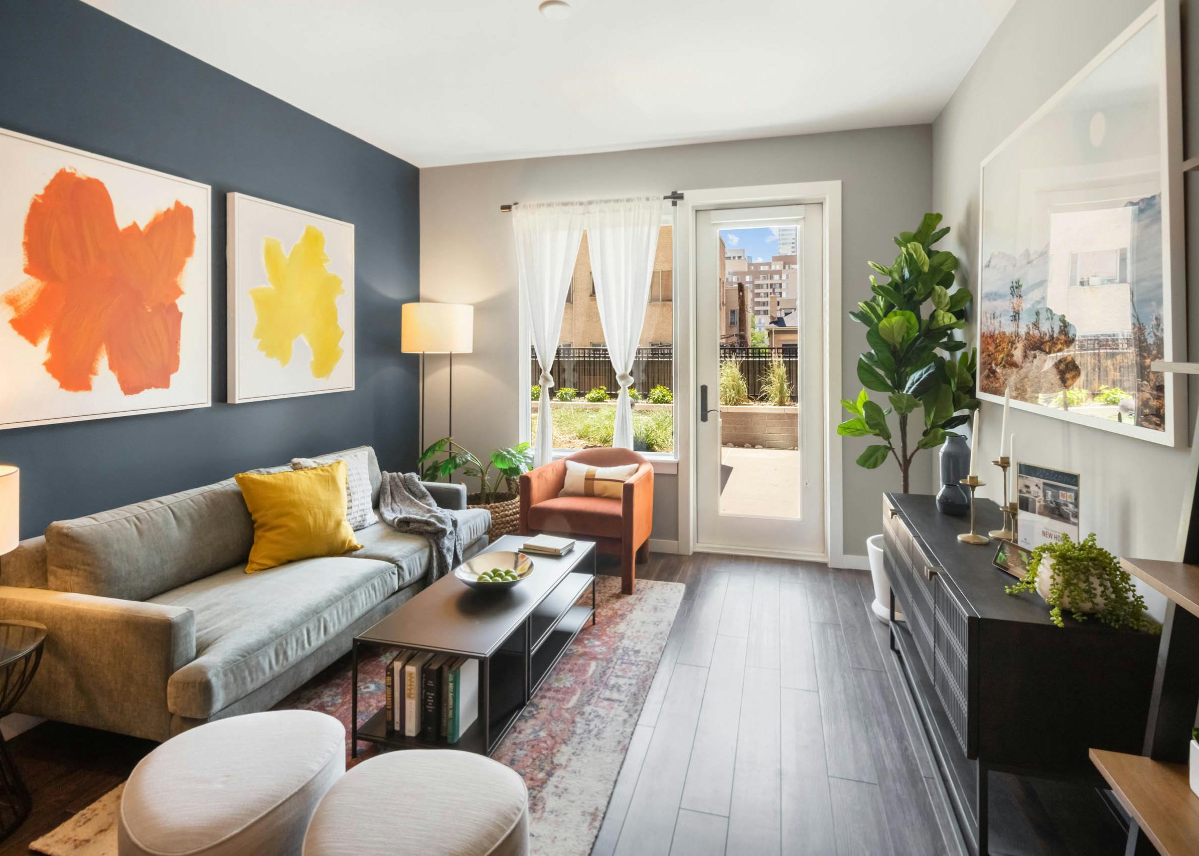 Bright AMLI at Uptown apartment living room with orange and yellow artwork on dark blue accent wall and door leading to patio