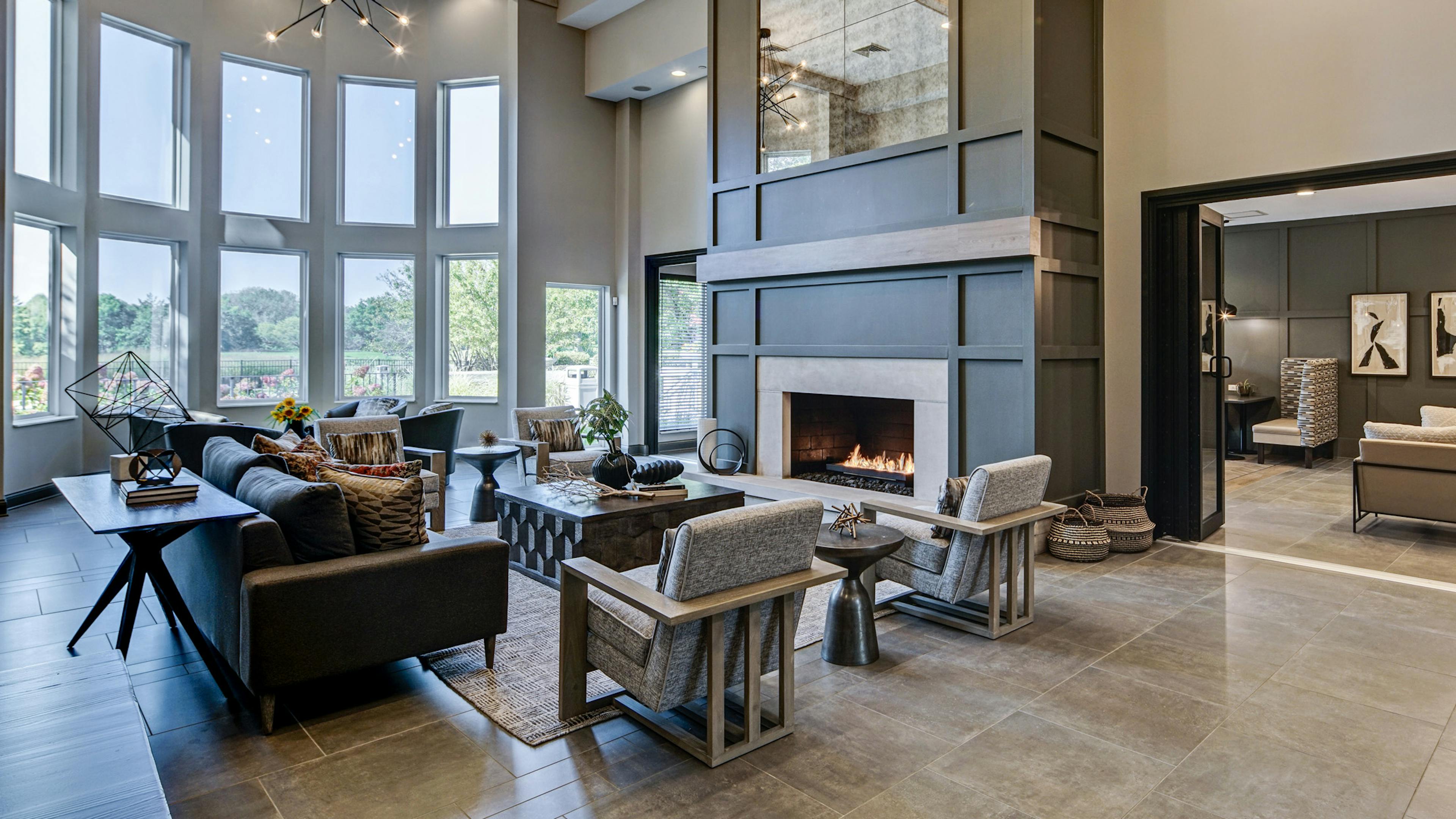 AMLI at Seven Bridges great room with modern gray décor with seating areas and two-story lit fireplace and wall of windows 