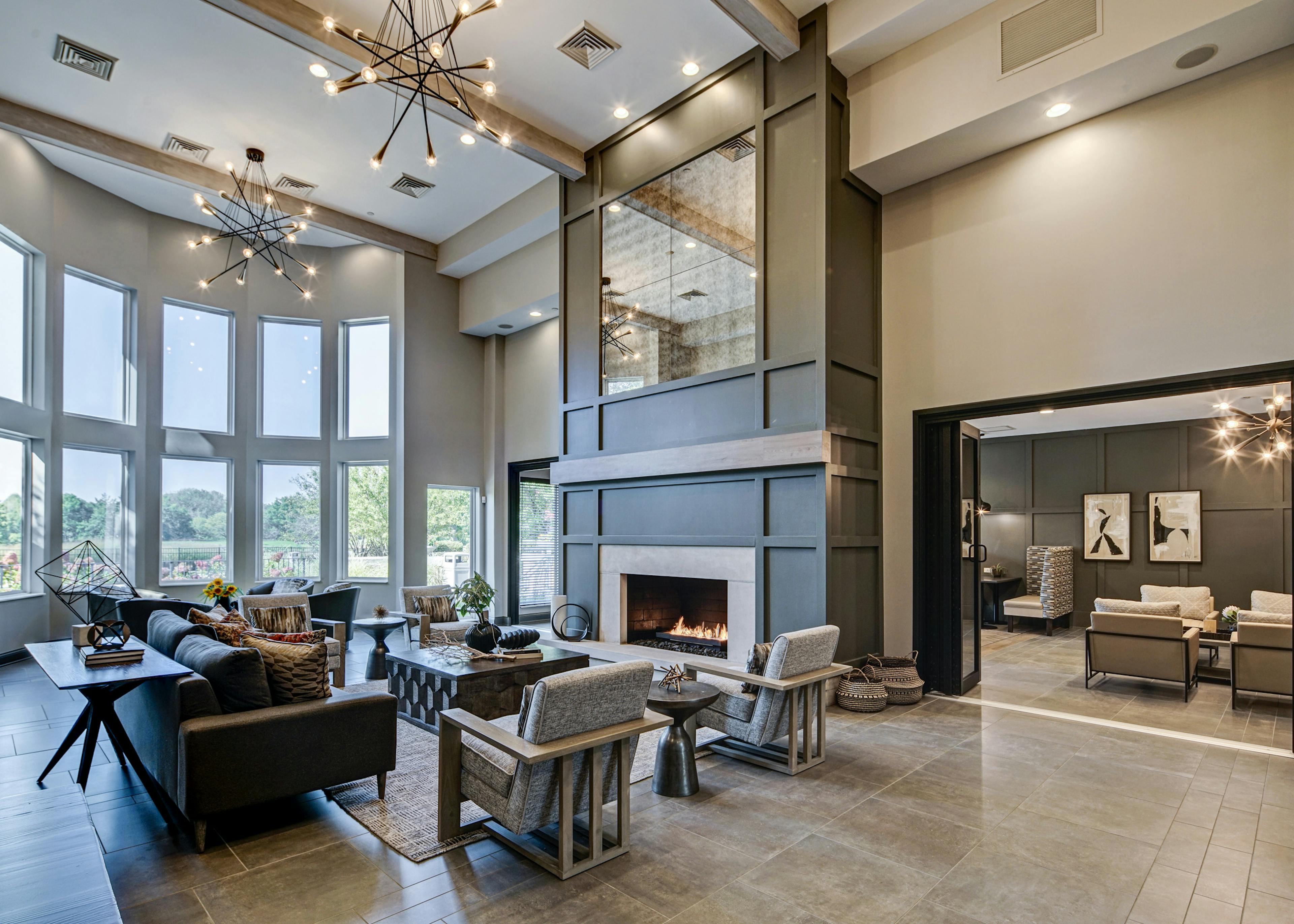 AMLI at Seven Bridges great room with modern gray décor with seating areas and two-story lit fireplace and wall of windows 
