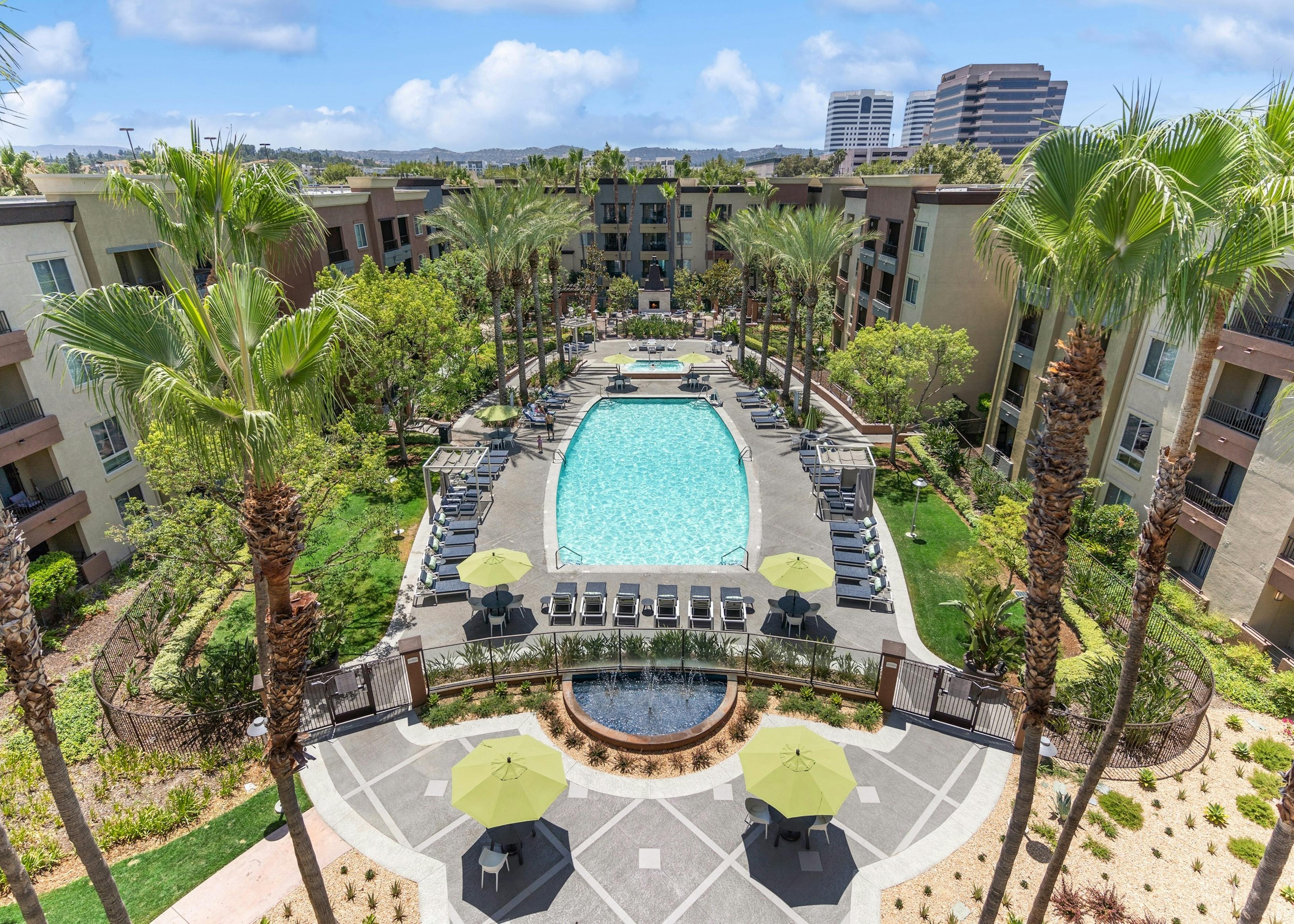 Aerial view of the AMLI Warner Center swimming pool surrounded by lounge chairs and palm trees with mountains in rear