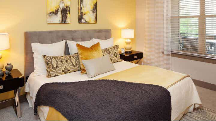 Bedroom at AMLI on Maple with a large white, yellow and brown bed against a yellow accent wall with a window to the right