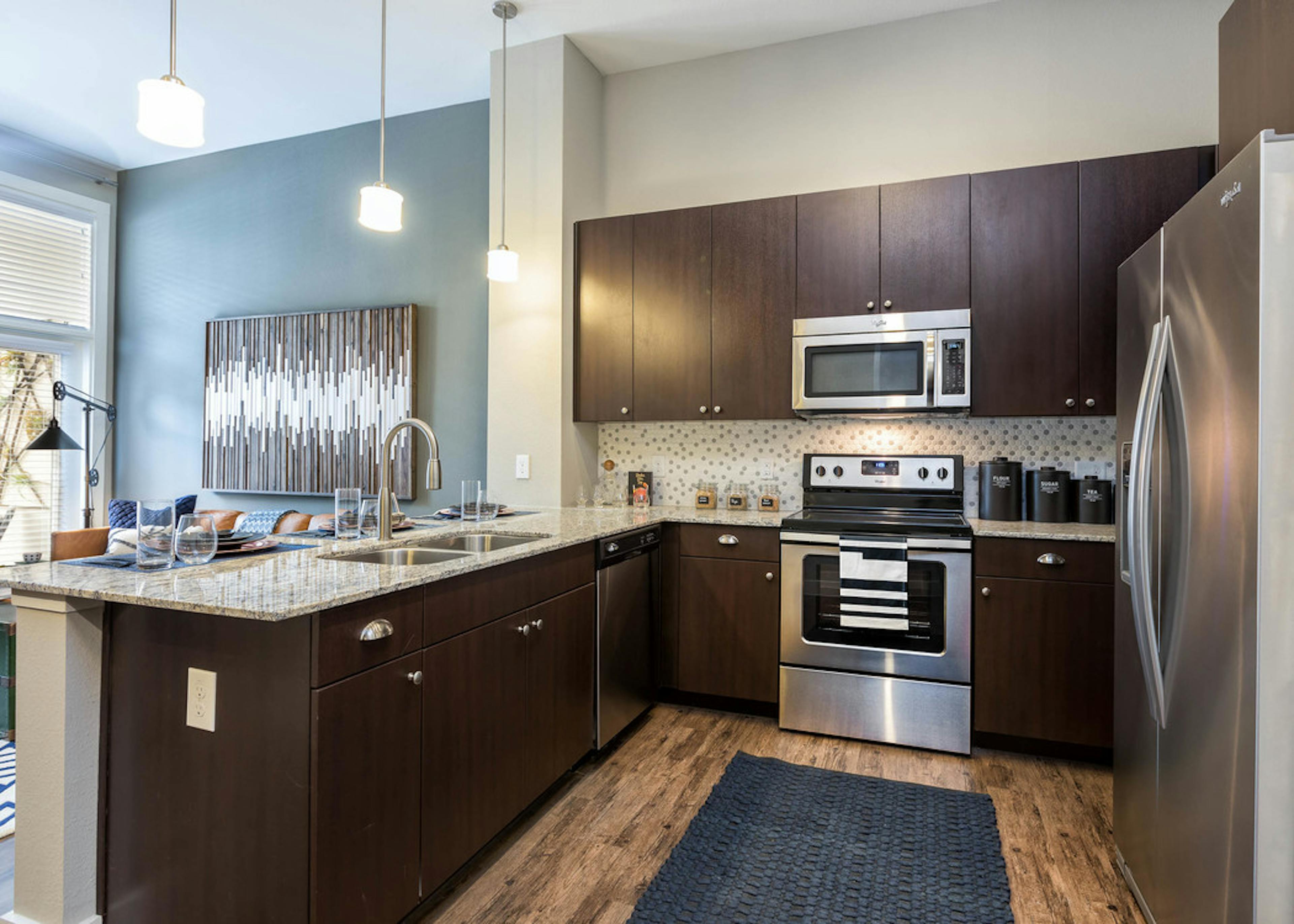 Interior of AMLI Frisco Crossing apartment kitchen with espresso cabinetry and tile backsplash and stainless steel appliances