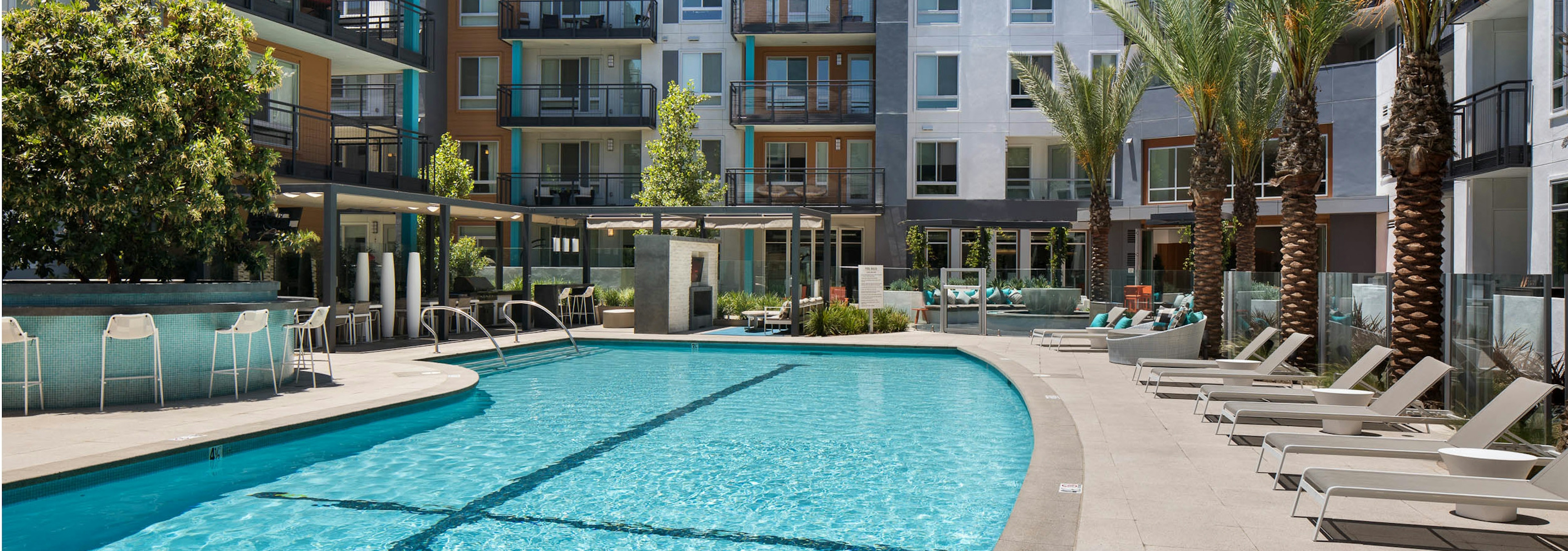 Daytime view of AMLI Uptown Orange swimming pool area with lounge seating and cabanas with individual TVs and palm trees