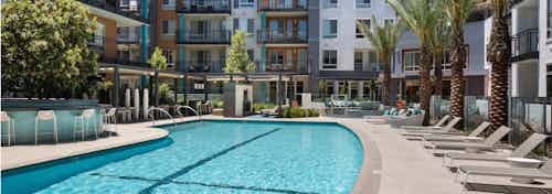 Daytime view of AMLI Uptown Orange swimming pool area with lounge seating and cabanas with individual TVs and palm trees