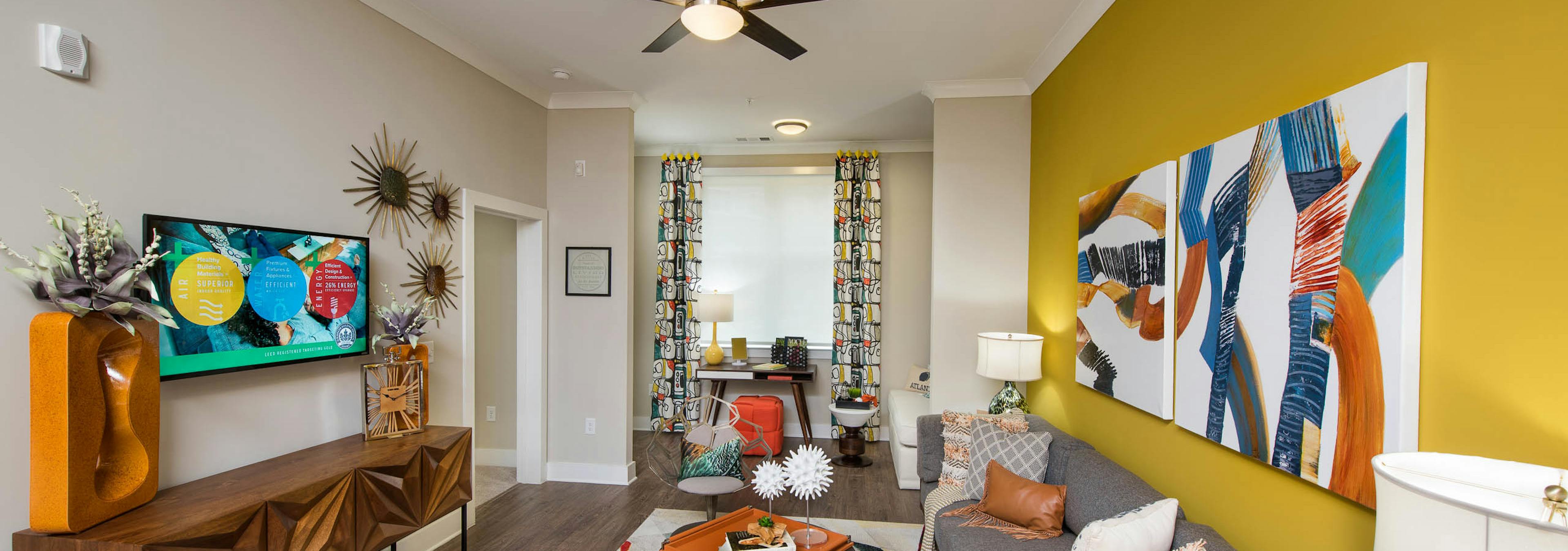 AMLI Buckhead living room with wood floors and a mustard yellow accent wall with bold modern styled orange and blue decor