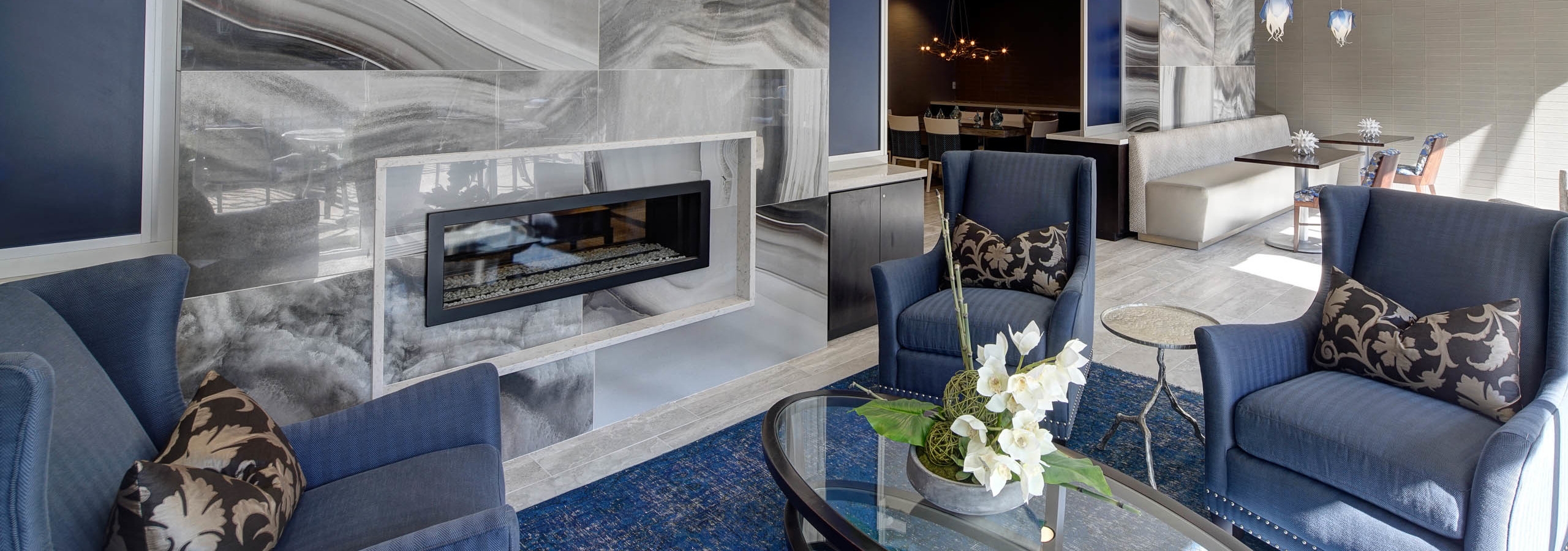 Lounge at AMLI Deerfield with a large marble fireplace and blue seating with tables and gourmet kitchen in background