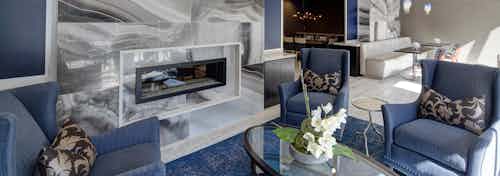 Lounge at AMLI Deerfield with a large marble fireplace and blue seating with tables and gourmet kitchen in background
