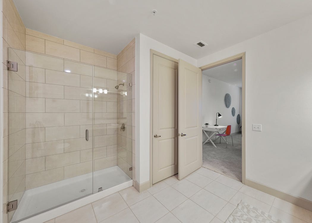 Interior view of AMLI 8800 apartment bathroom with large seamless glass shower enclosure and white ceramic tile floor