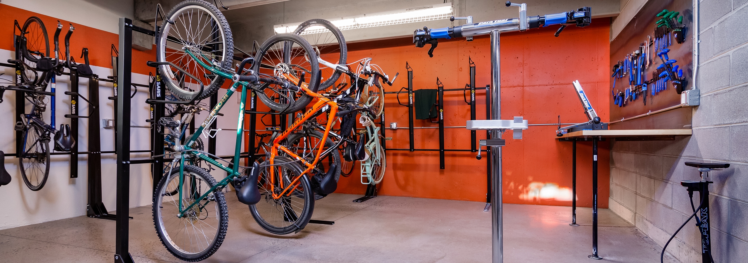 Interior of AMLI Littleton Village Bike/ski/snowboard repair room with orange walls, bike racks and tools and work counter
