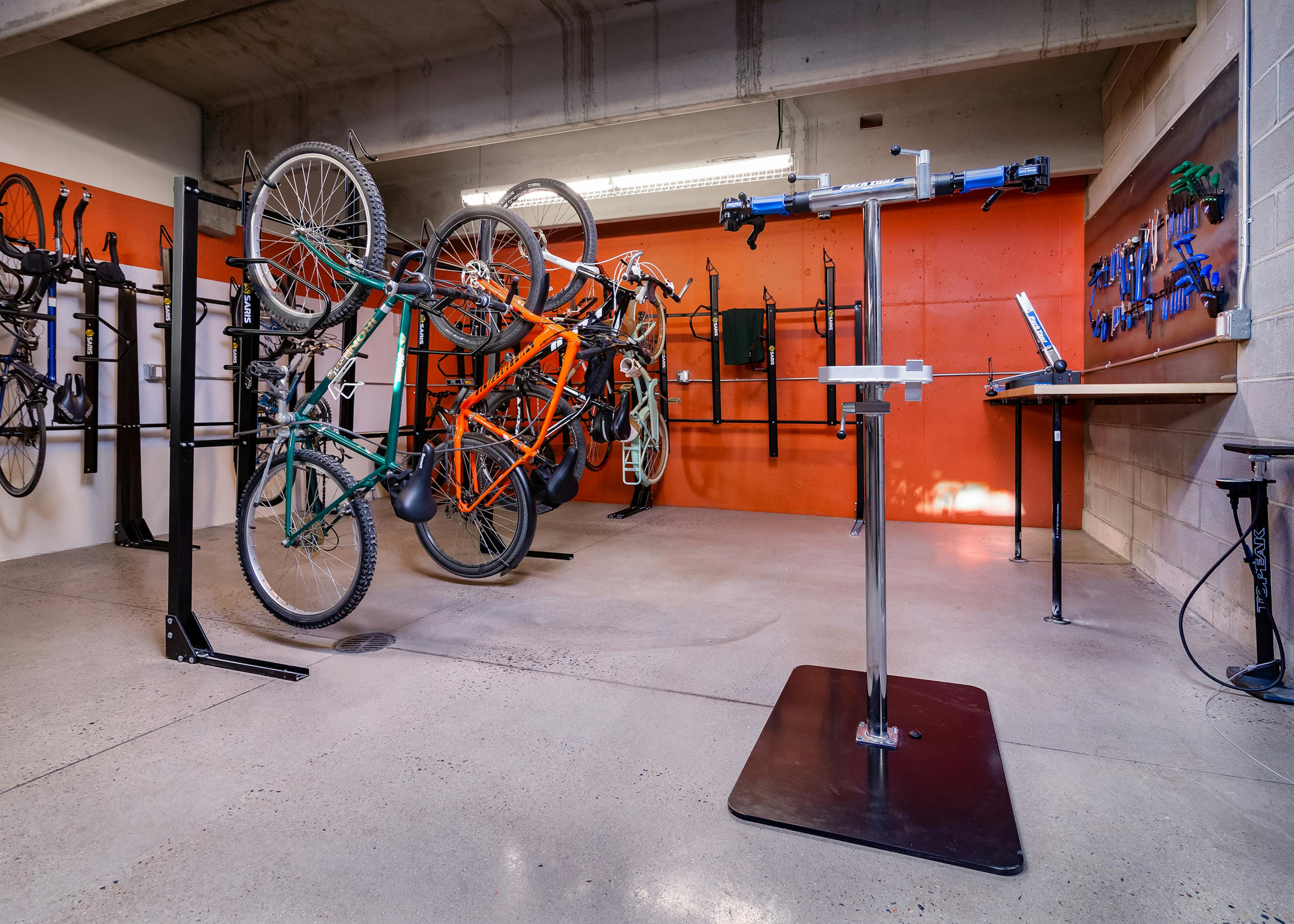 Interior of AMLI Littleton Village Bike/ski/snowboard repair room with orange walls, bike racks and tools and work counter