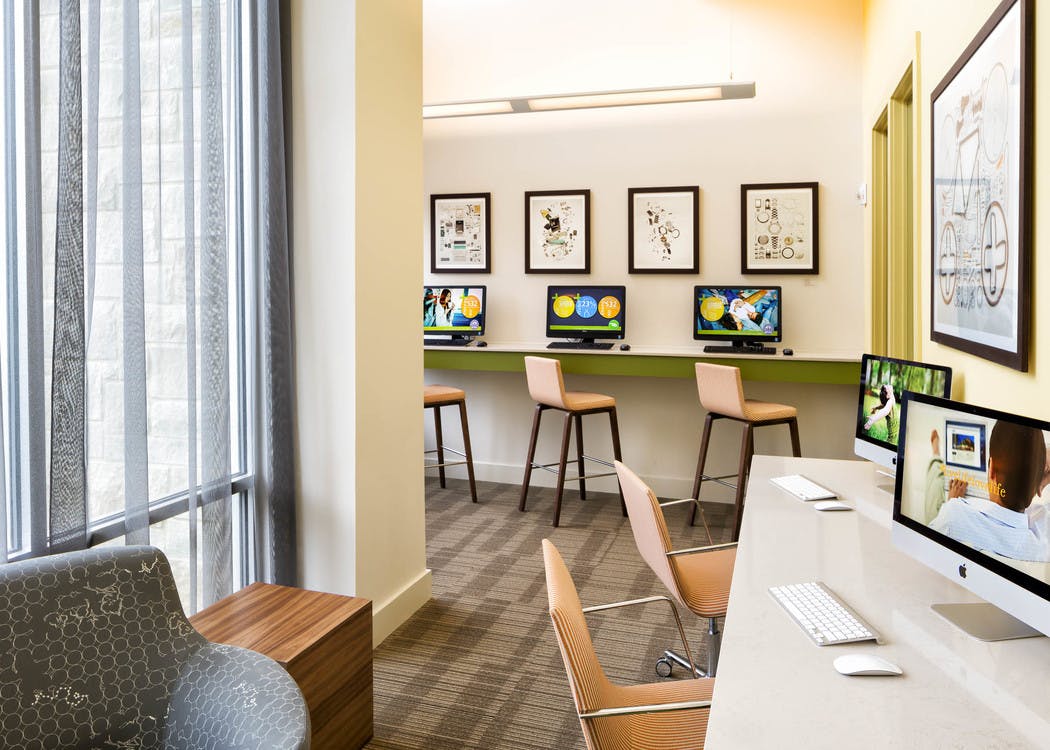 AMLI at Mueller business center with bar stools at a raised counter with desktop computers and light flooring with tall windows