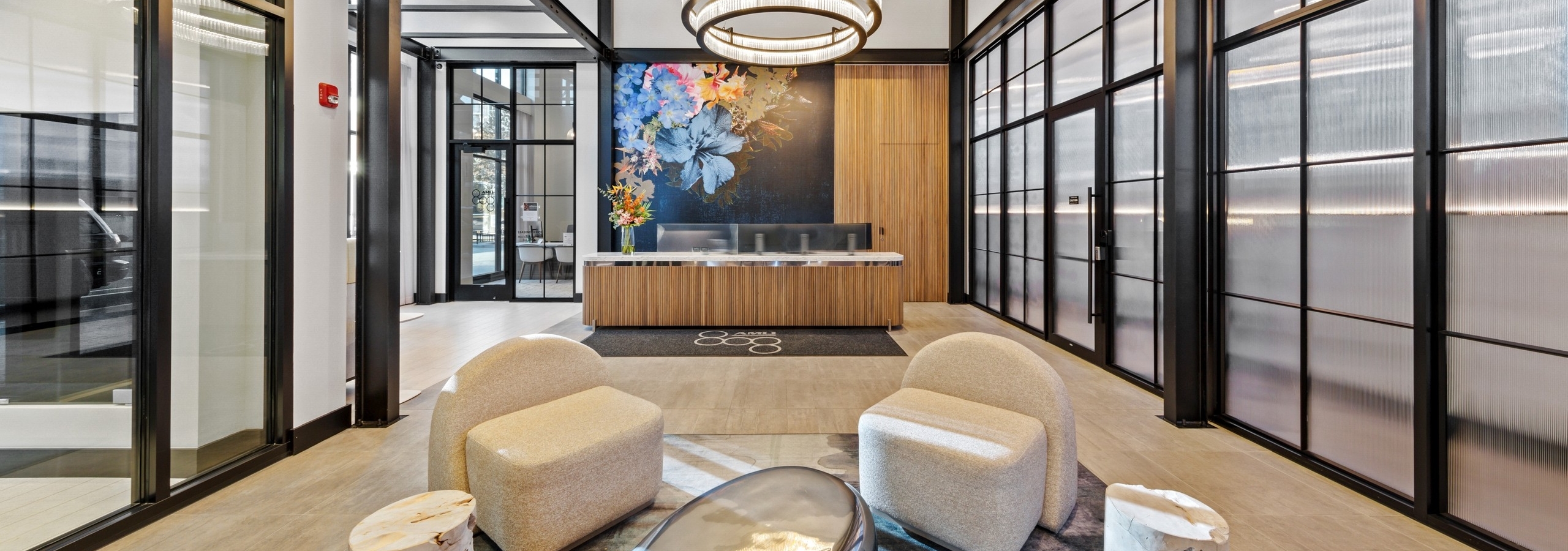 AMLI 808 lobby with beige chairs surrounding bold side tables on a modern grey rug with view of reception desk in background