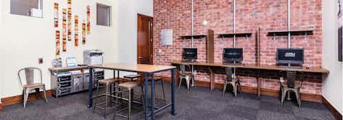 A business center at AMLI Park Avenue apartments with computers and chairs up against a brick wall with a printer and table