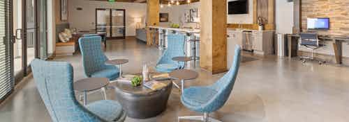 AMLI Old 4th Ward newly renovated clubroom with kitchen and long tables with stools as well as comfortable blue lounge chairs