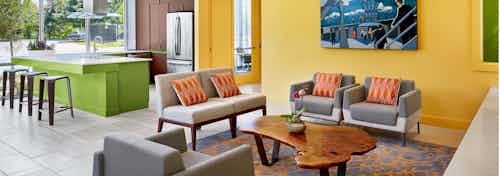 AMLI at Mueller clubroom with grey couches and chairs against a yellow wall with barstools at a green counter in background