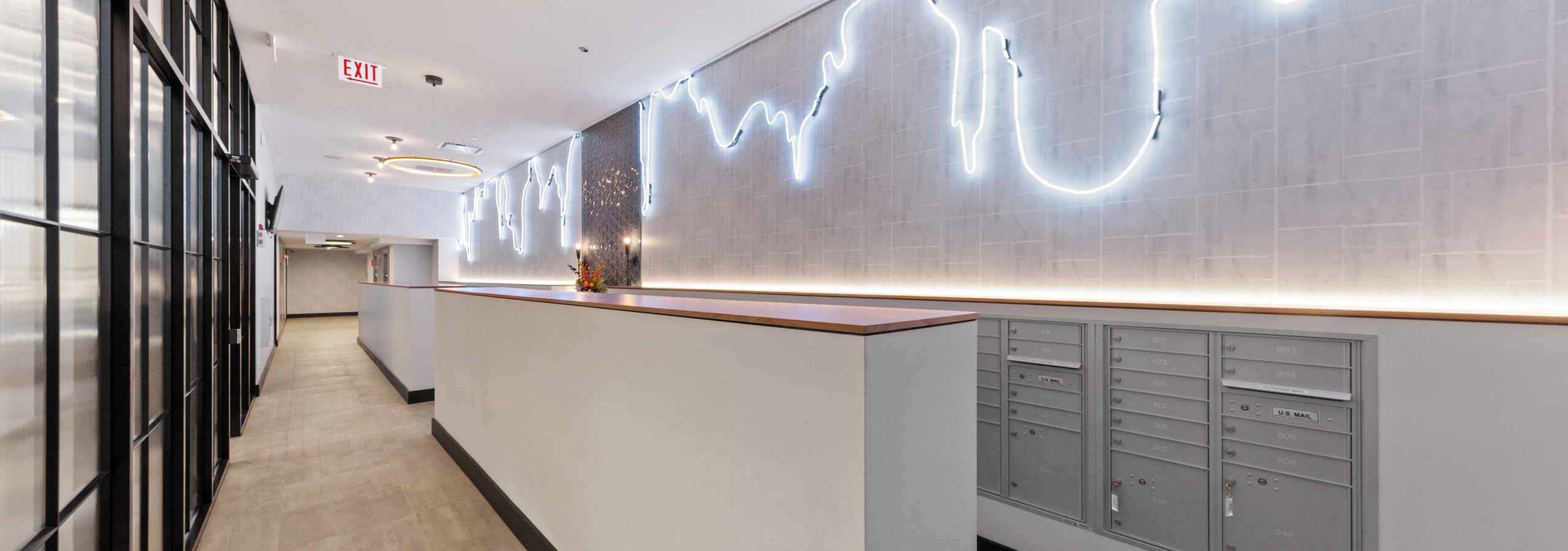 AMLI 808 mailroom featuring grey mail boxes and beige flooring with unique lights lining the full length of light grey walls