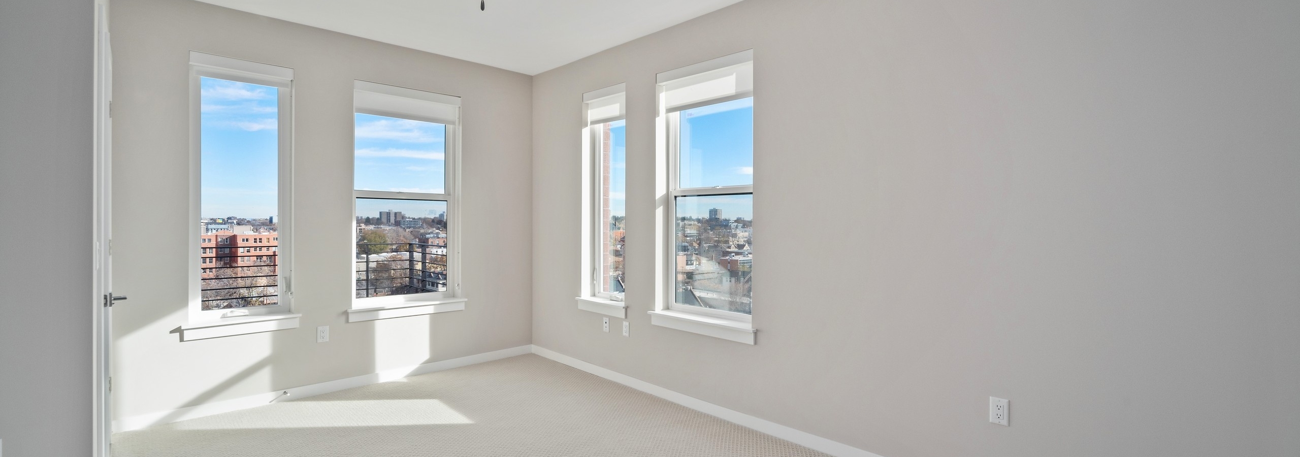 Empty AMLI at Uptown apartment bedroom with neutral carpet  and light grey walls with four windows letting in natural light