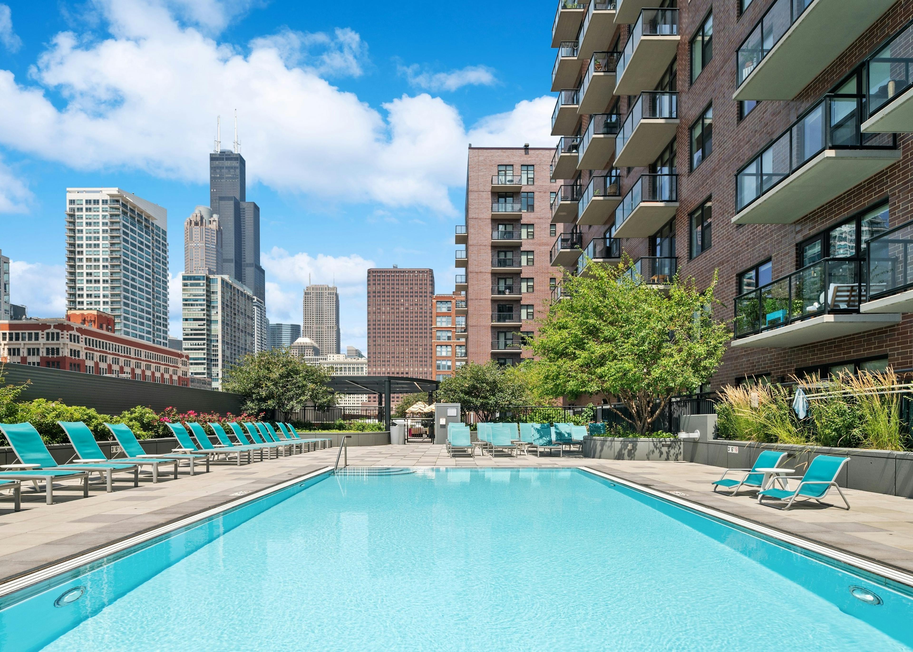 AMLI Lofts resort style swimming pool with blue lounge chairs and lush greenery with view of city skyline in background