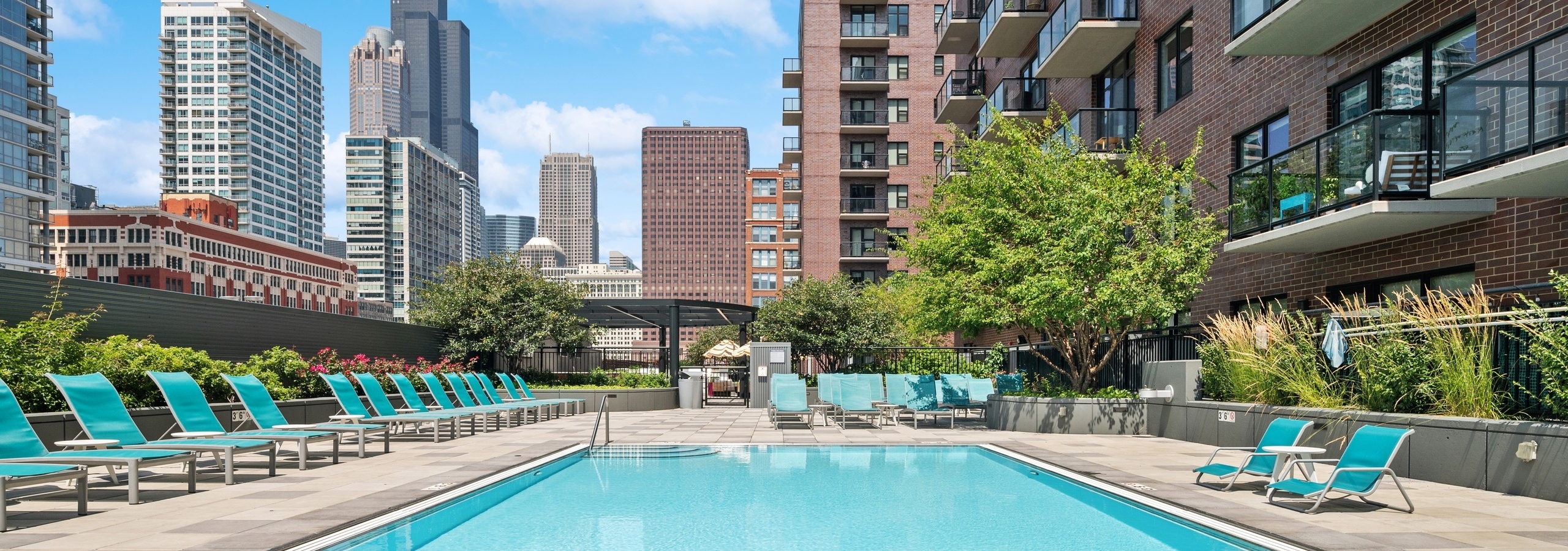 AMLI Lofts resort style swimming pool with blue lounge chairs and lush greenery with view of city skyline in background