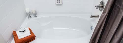 A bathroom shower tub at AMLI Arista apartments with towels and candles and soap as well as white tile and a shower curtain