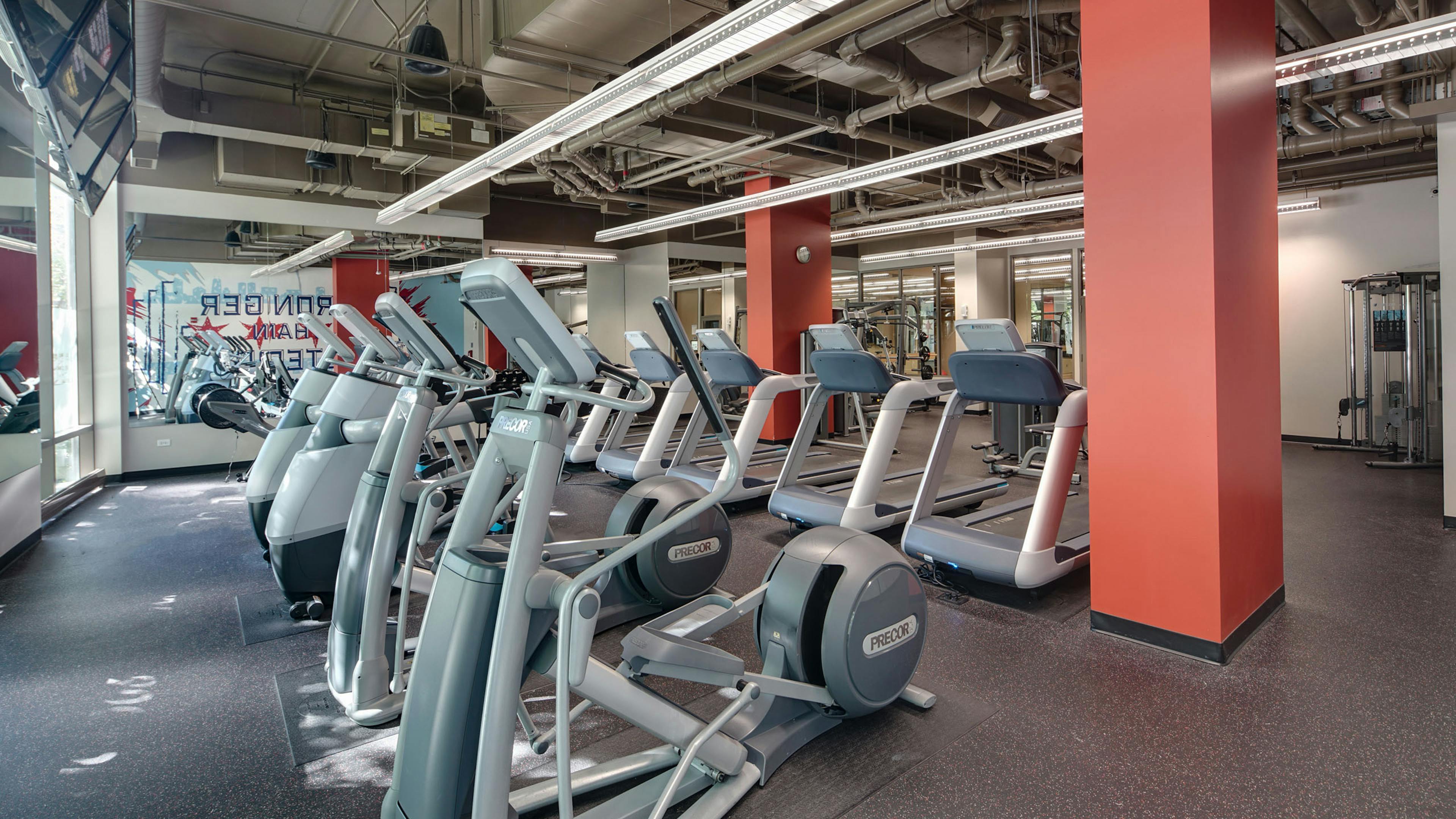 AMLI 900 fitness center featuring treadmills and elliptical machines with loft ceiling and Chicago themed mural in background