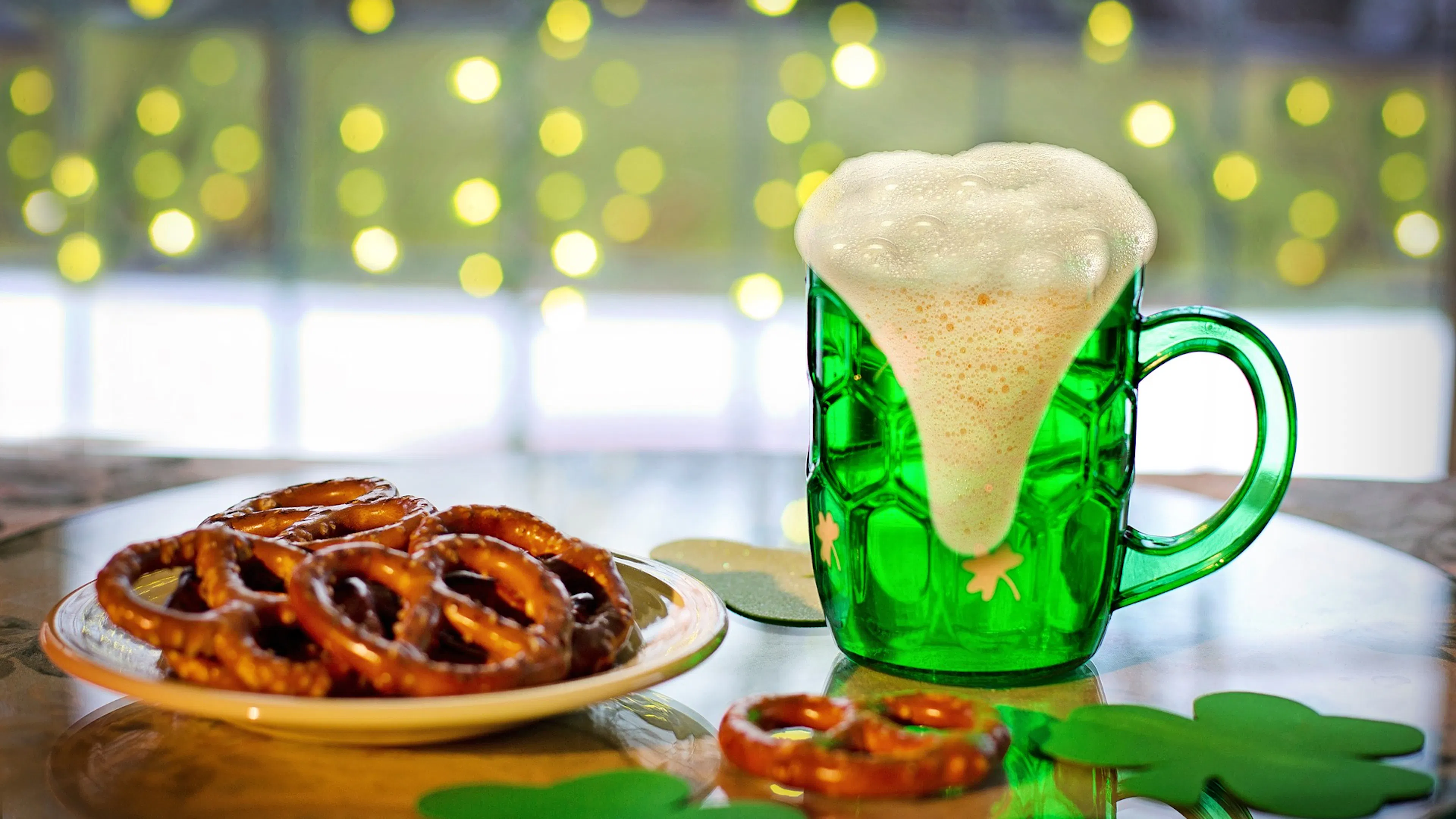 green beer with froth dripping down and a plate of pretzels beside it