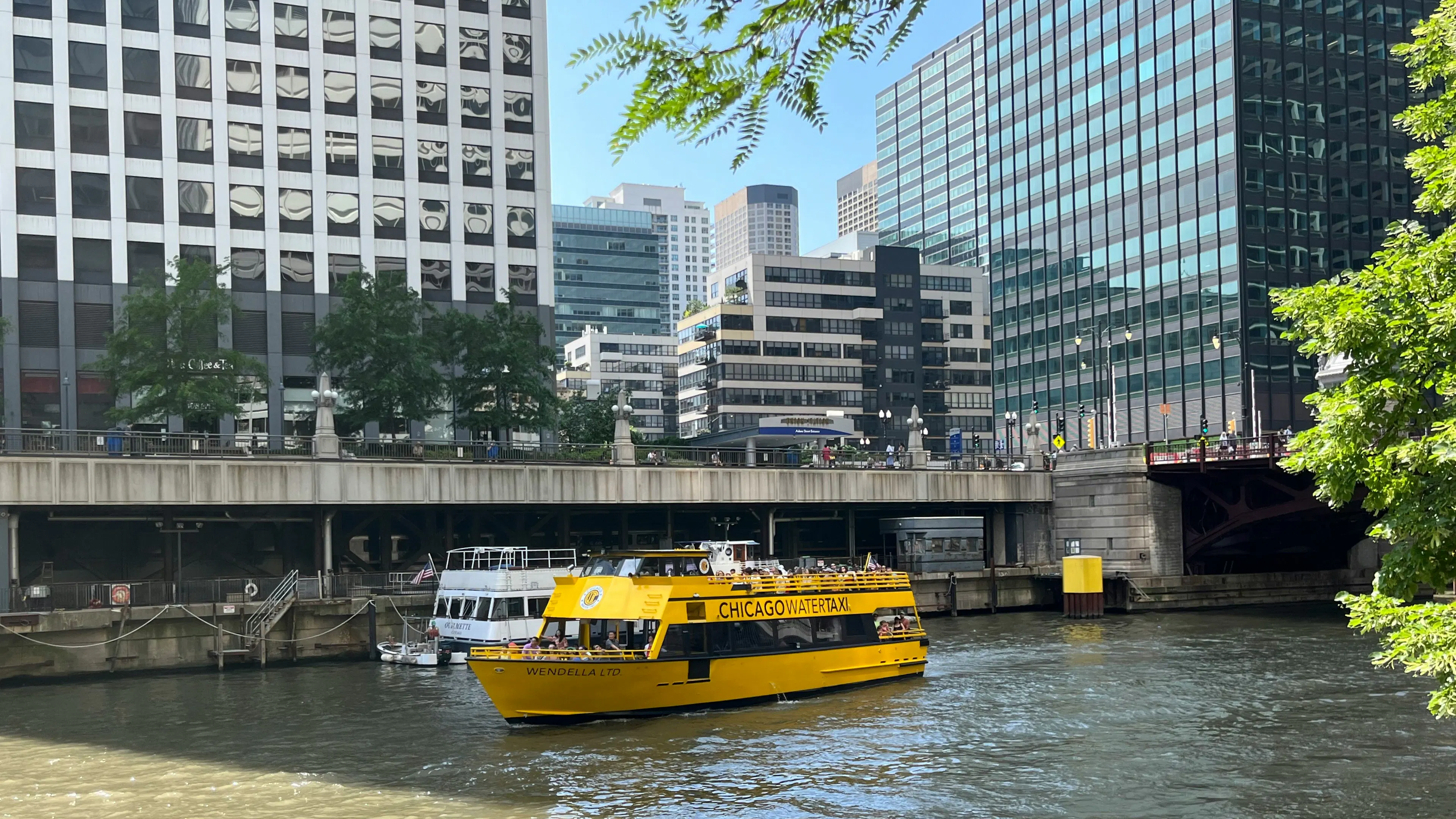 A yellow Chicago Water Taxi boat floating past a white boat on the Chicago River surrounded by buildings