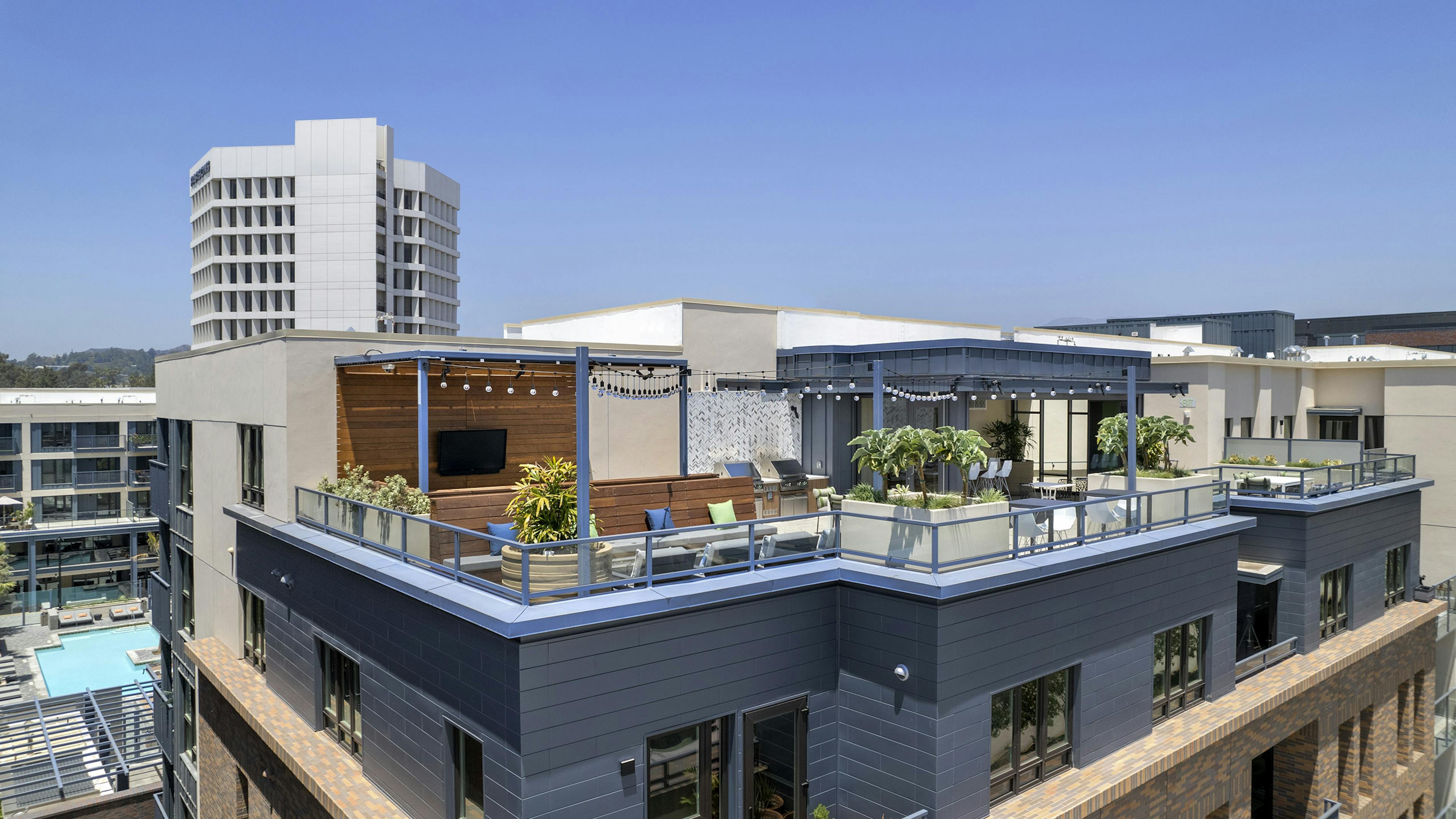 Daytime view of rooftop sky deck with various lounge seating and big screen TV and decorative planters at AMLI Old Pasadena