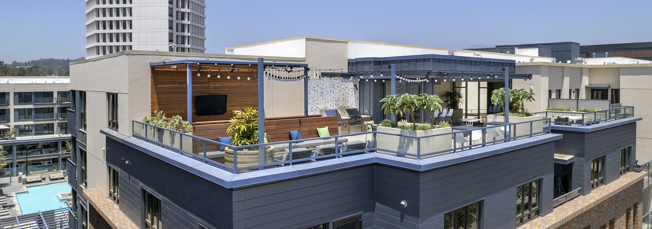 Daytime view of rooftop sky deck with various lounge seating and big screen TV and decorative planters at AMLI Old Pasadena