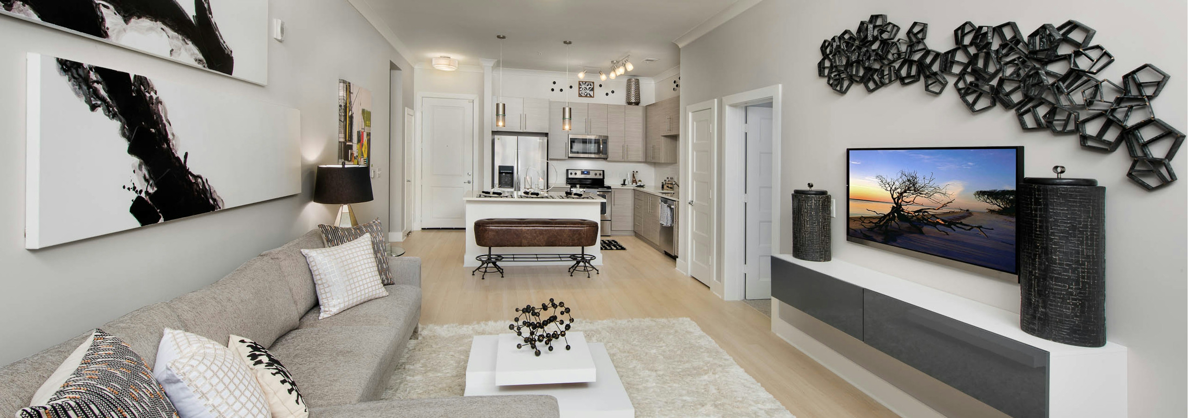 Living room at AMLI Buckhead with a beige couch and black and white wall decor with light wood floors leading to kitchen area