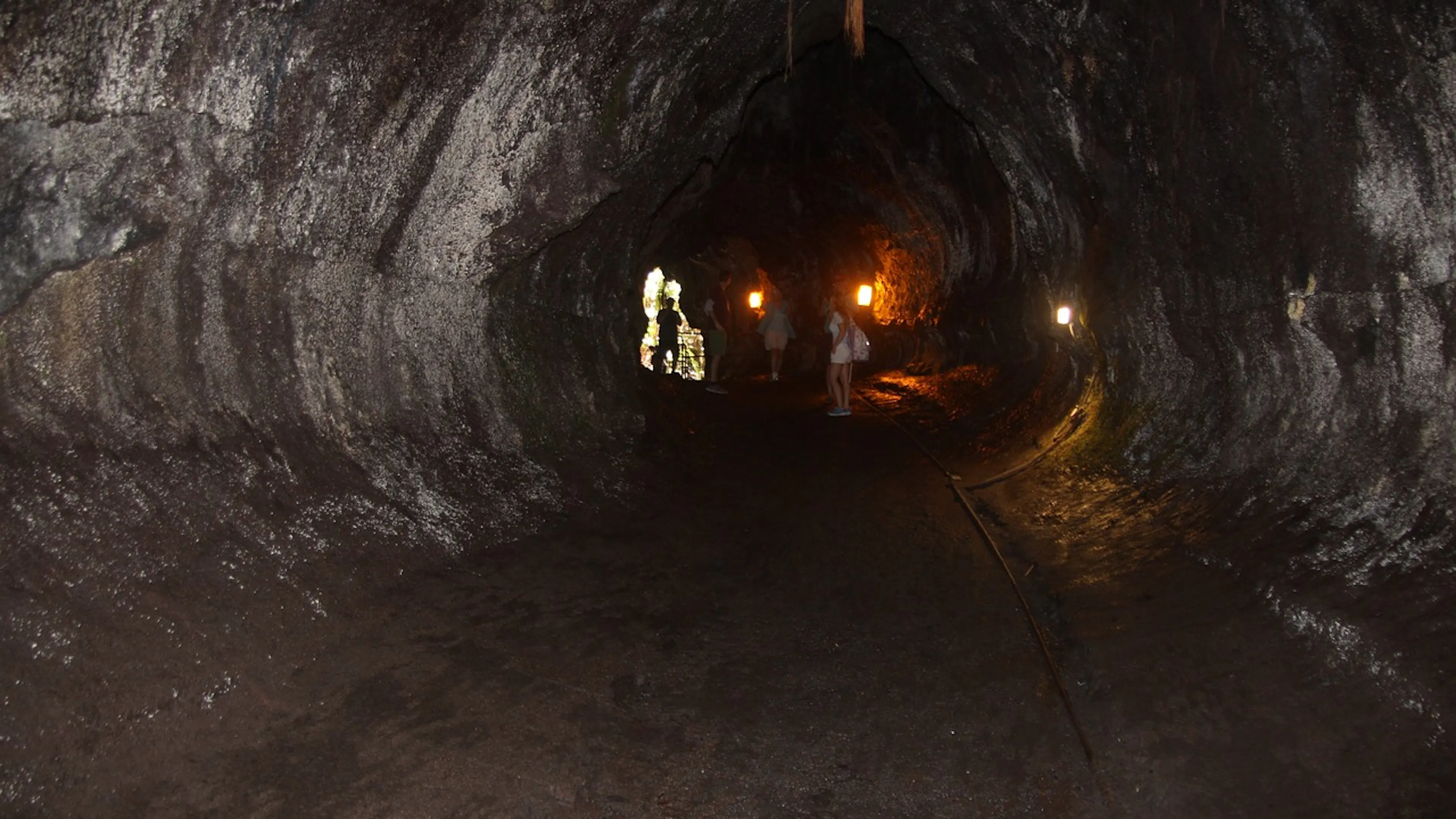 A group of hikers near the entrance to a lava tube cave lit by mining lights