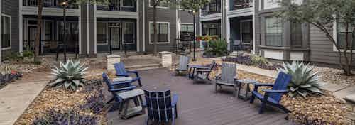 Day view of courtyard at AMLI Eastside apartments with gray and blue Adirondack chairs on a deck with trees and landscaping
