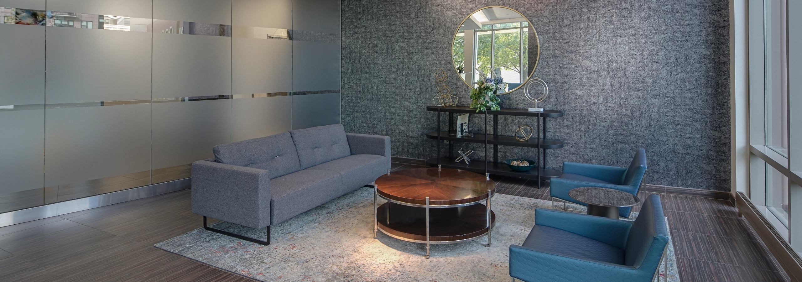 The lobby at AMLI 900 which displays a bold grey printed accent wall paired with blue furnishings and a frosted glass wall